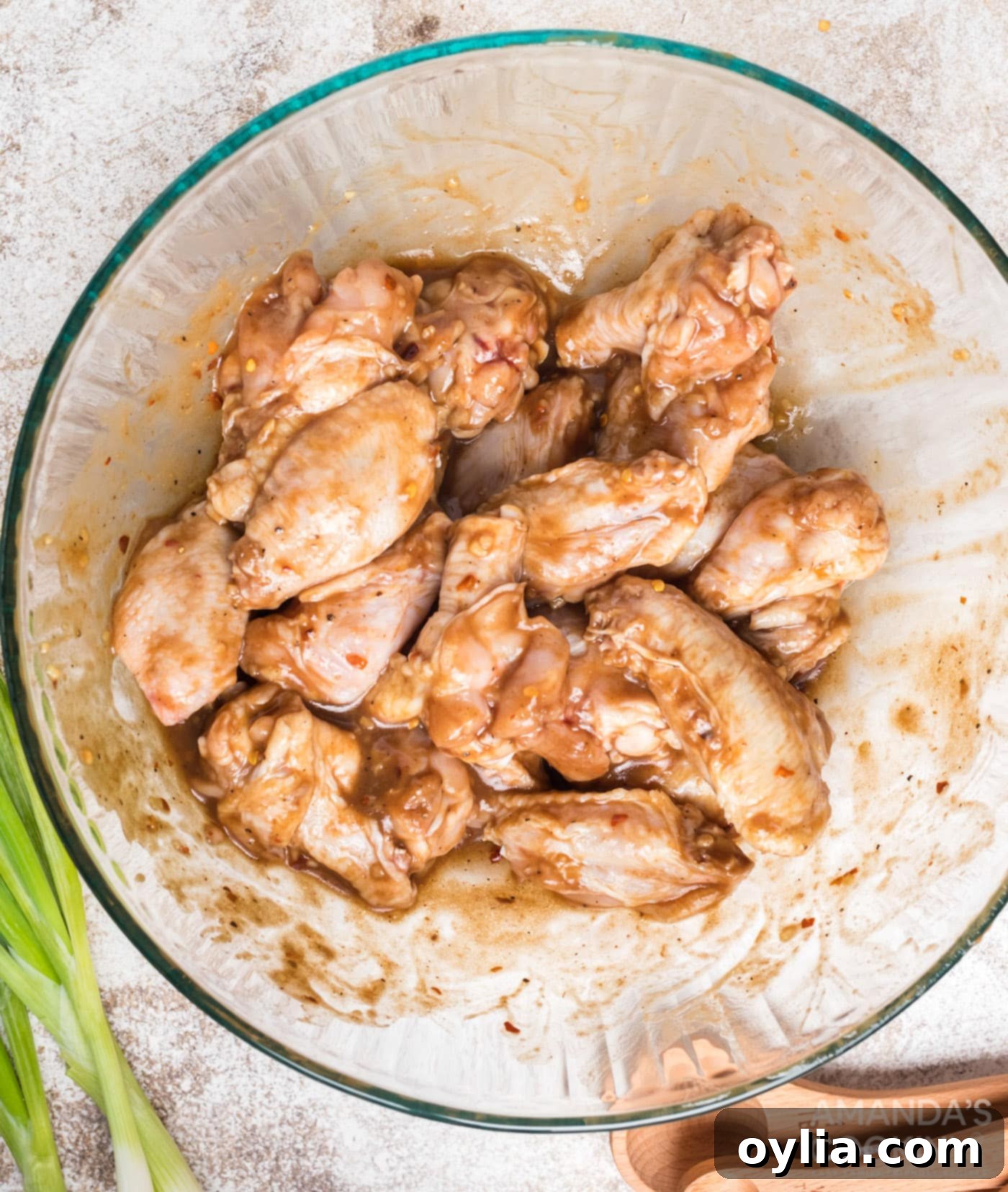 Chicken wings being tossed in a large bowl with the spicy marinade until fully coated.