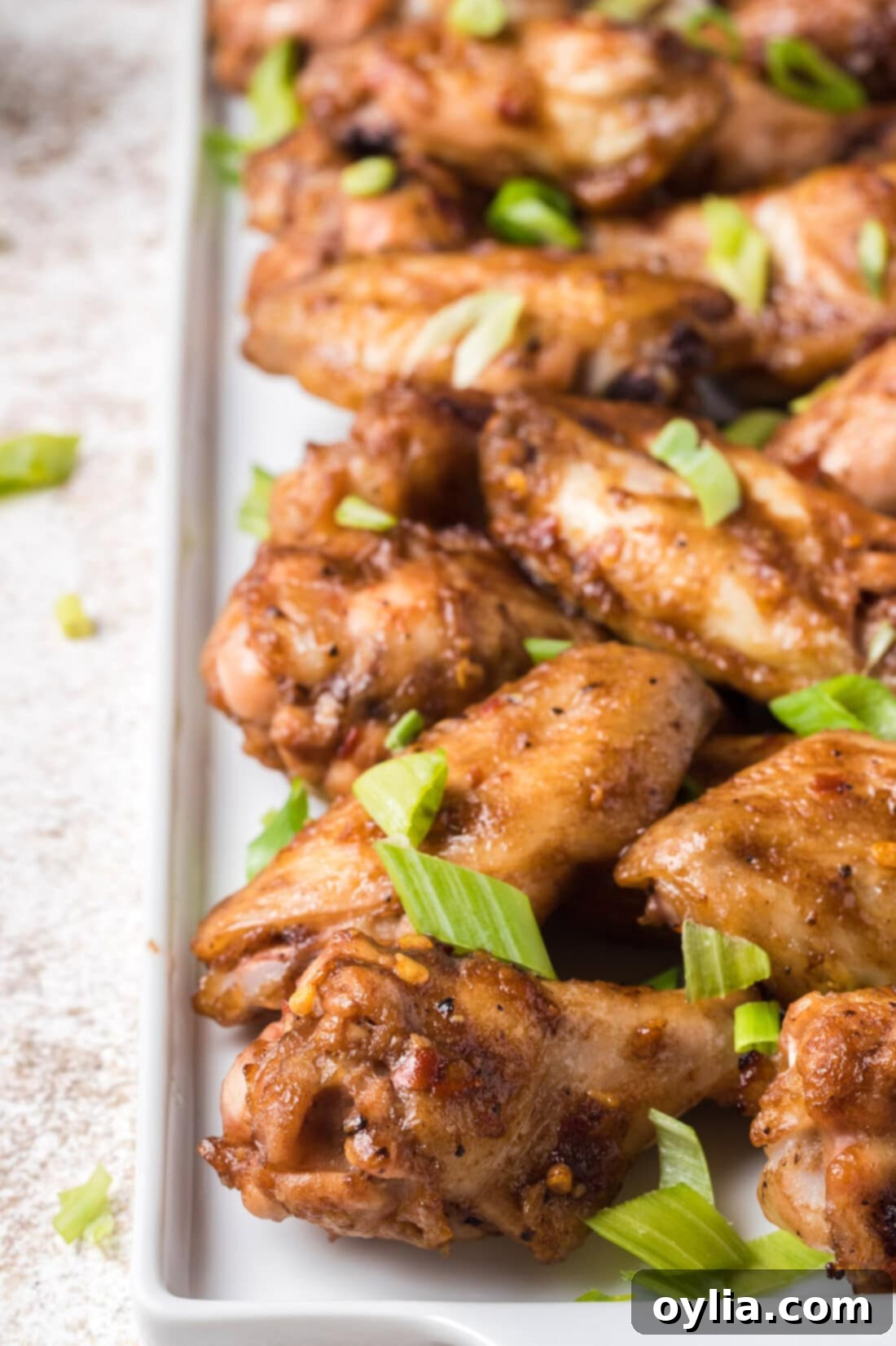 A large platter of freshly baked spicy sticky chicken wings, garnished with green onions.