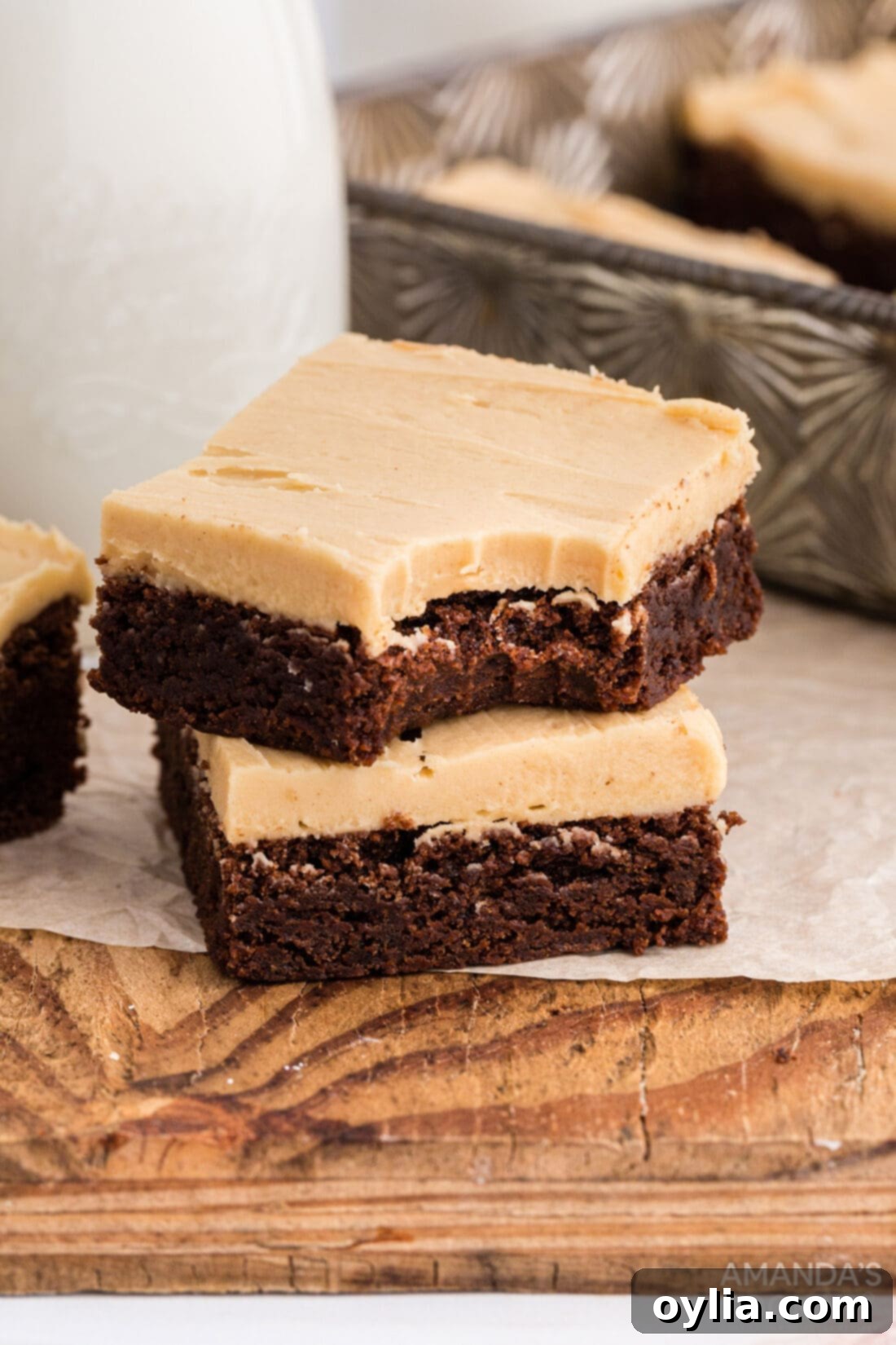 Two peanut butter frosted brownies, one with a bite taken, showcasing the fudgy texture