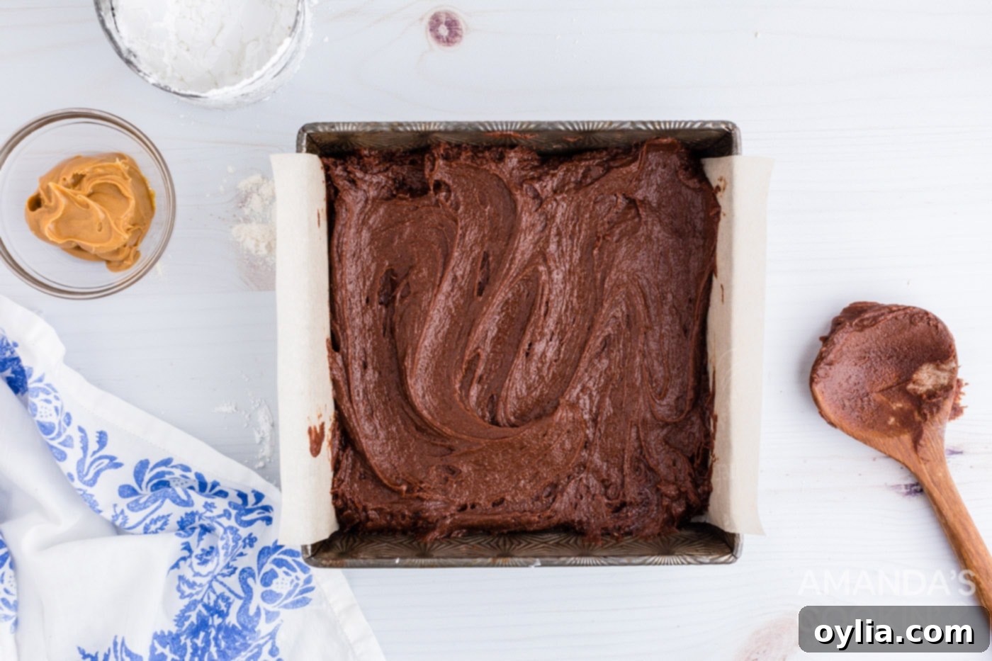 Smooth brownie batter spread evenly in a parchment-lined 8x8 baking pan
