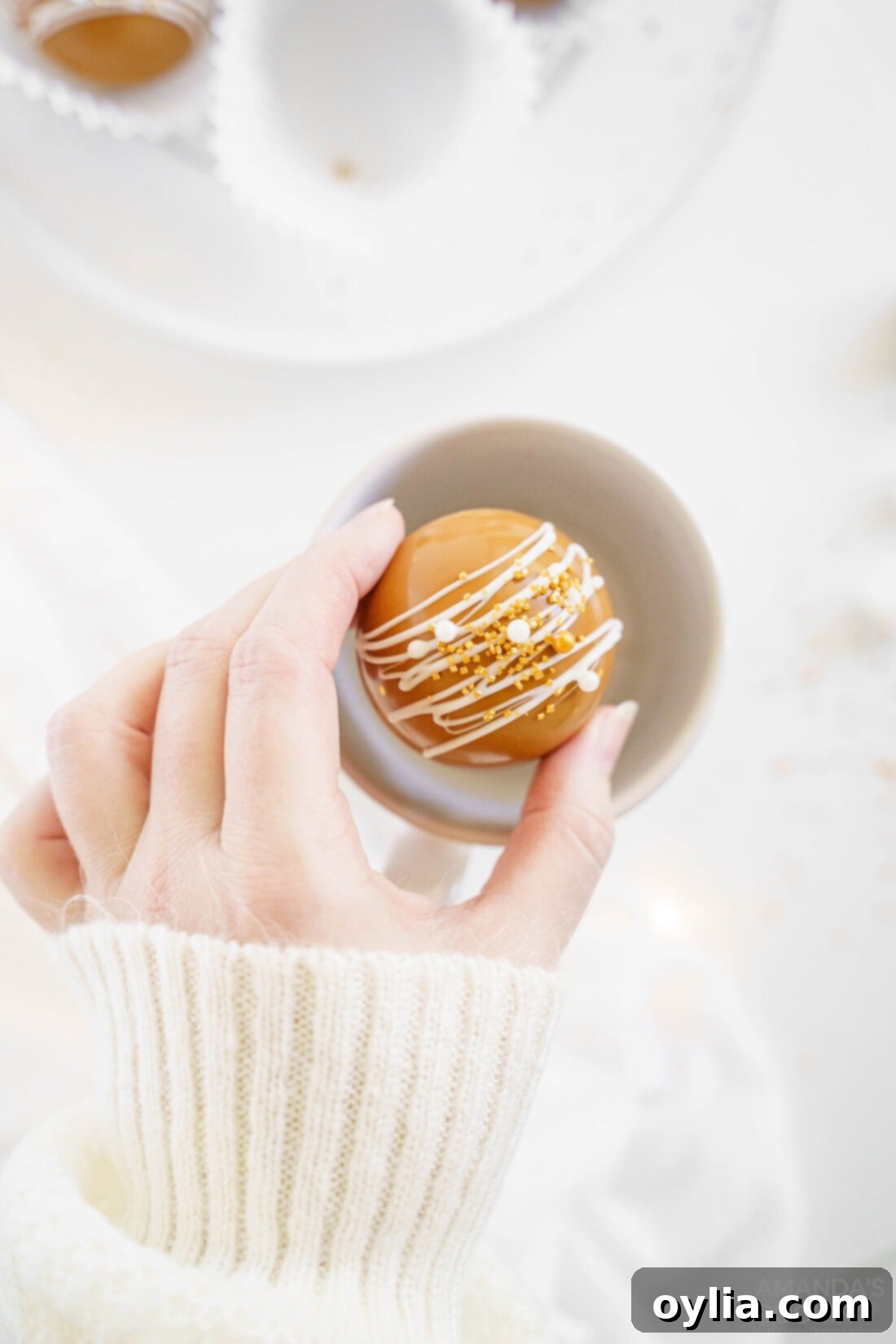 Woman placing a homemade caramel hot cocoa bomb into a mug, ready to be dissolved for a warm drink.