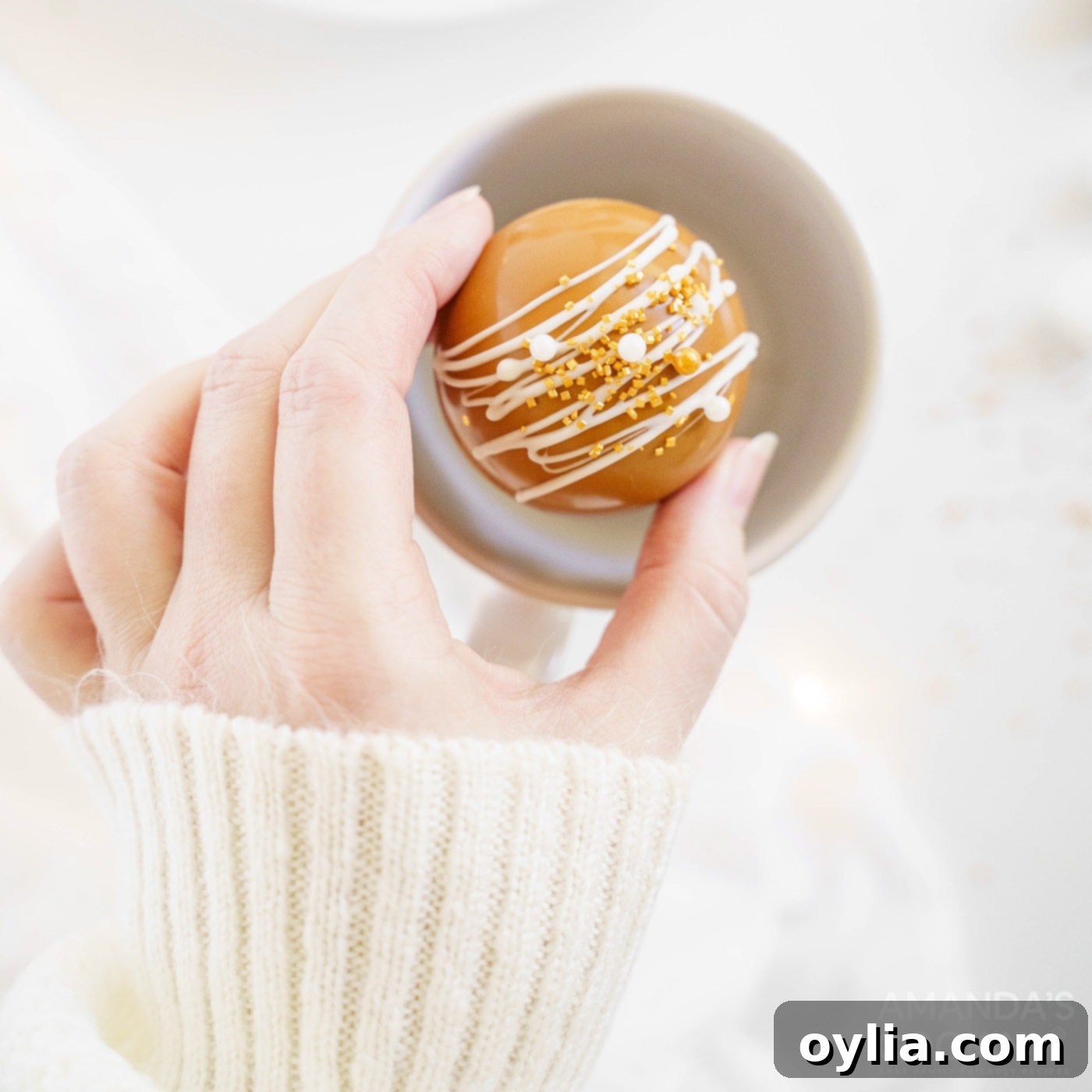 A hot cocoa bomb being carefully placed into a festive mug, ready for the hot milk.