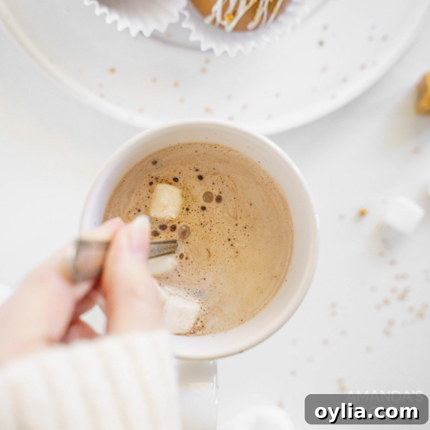 A spoon stirring a mug of hot cocoa, demonstrating the final step to combine all ingredients after the bomb has melted.