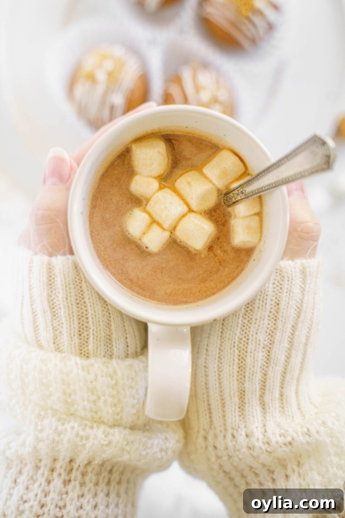 A woman smiling as she holds a mug of hot cocoa, enjoying the caramel hot chocolate bomb experience.