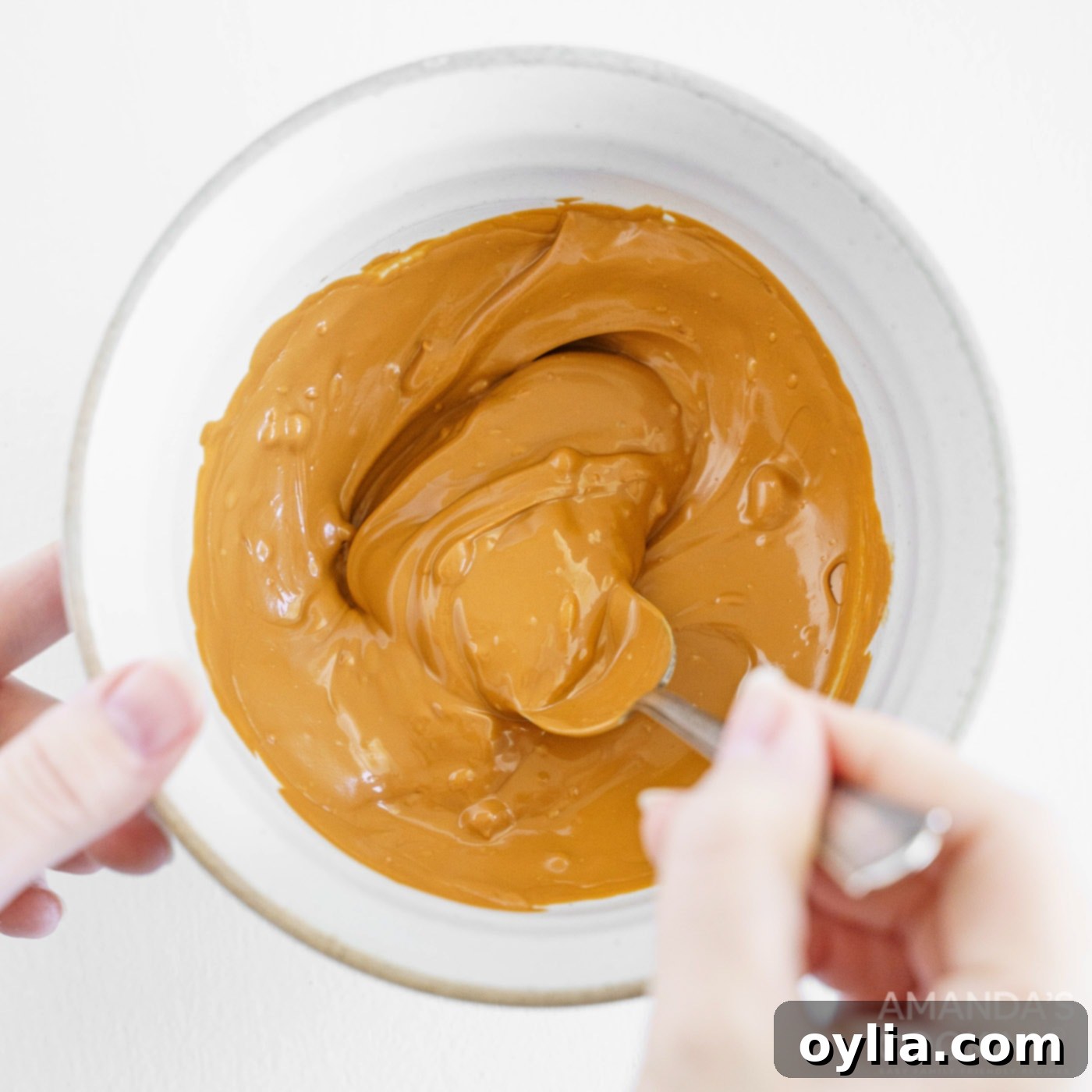 A close-up shot of a whisk stirring smooth, melted caramel candy melts in a bowl, demonstrating the first step in making hot cocoa bombs.