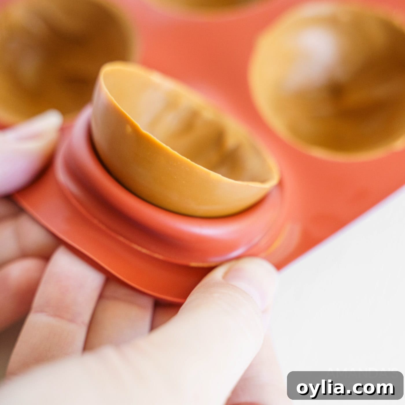 A hand gently removing a caramel candy half-sphere from a silicone mold, showing its perfectly rounded shape.