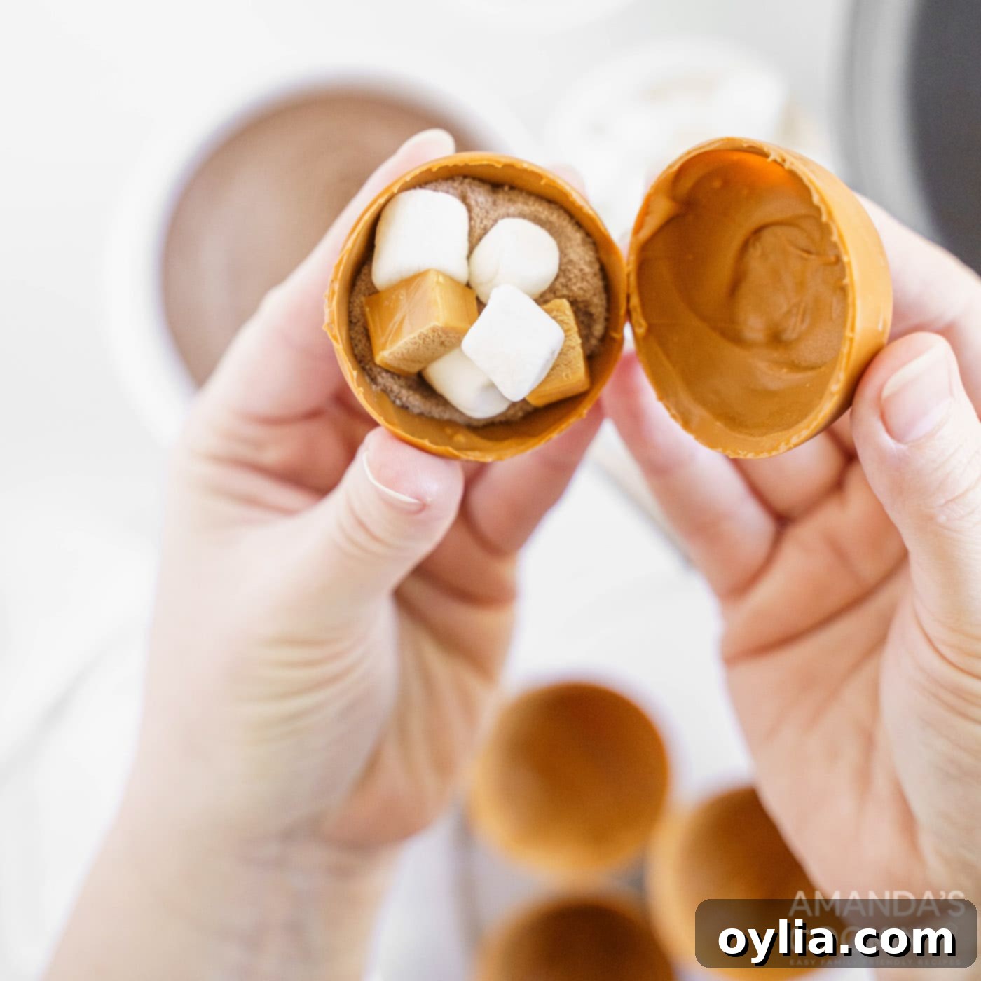 Hands carefully pressing two caramel candy half-spheres together to form a whole hot cocoa bomb, sealing the edges.