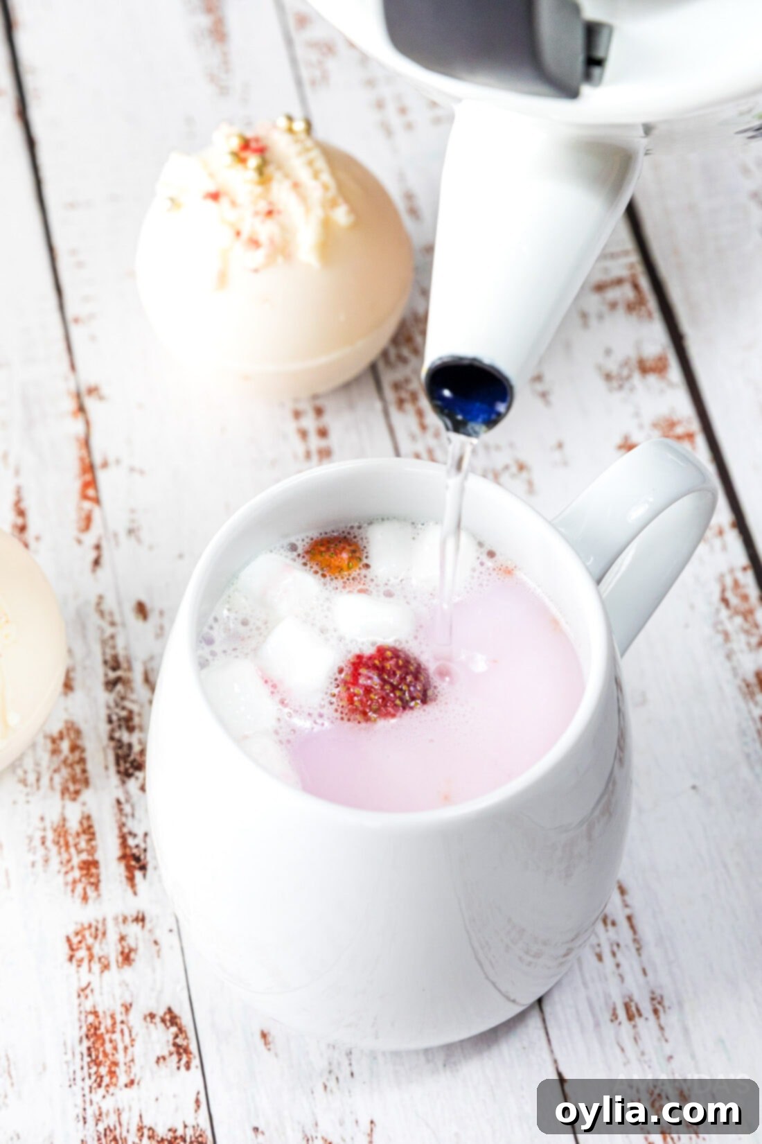 Indulgent Strawberry White Chocolate Hot Cocoa Bombs 15 Hot water being poured into a mug with a strawberry white chocolate hot cocoa bomb, creating a swirling pink and white drink.