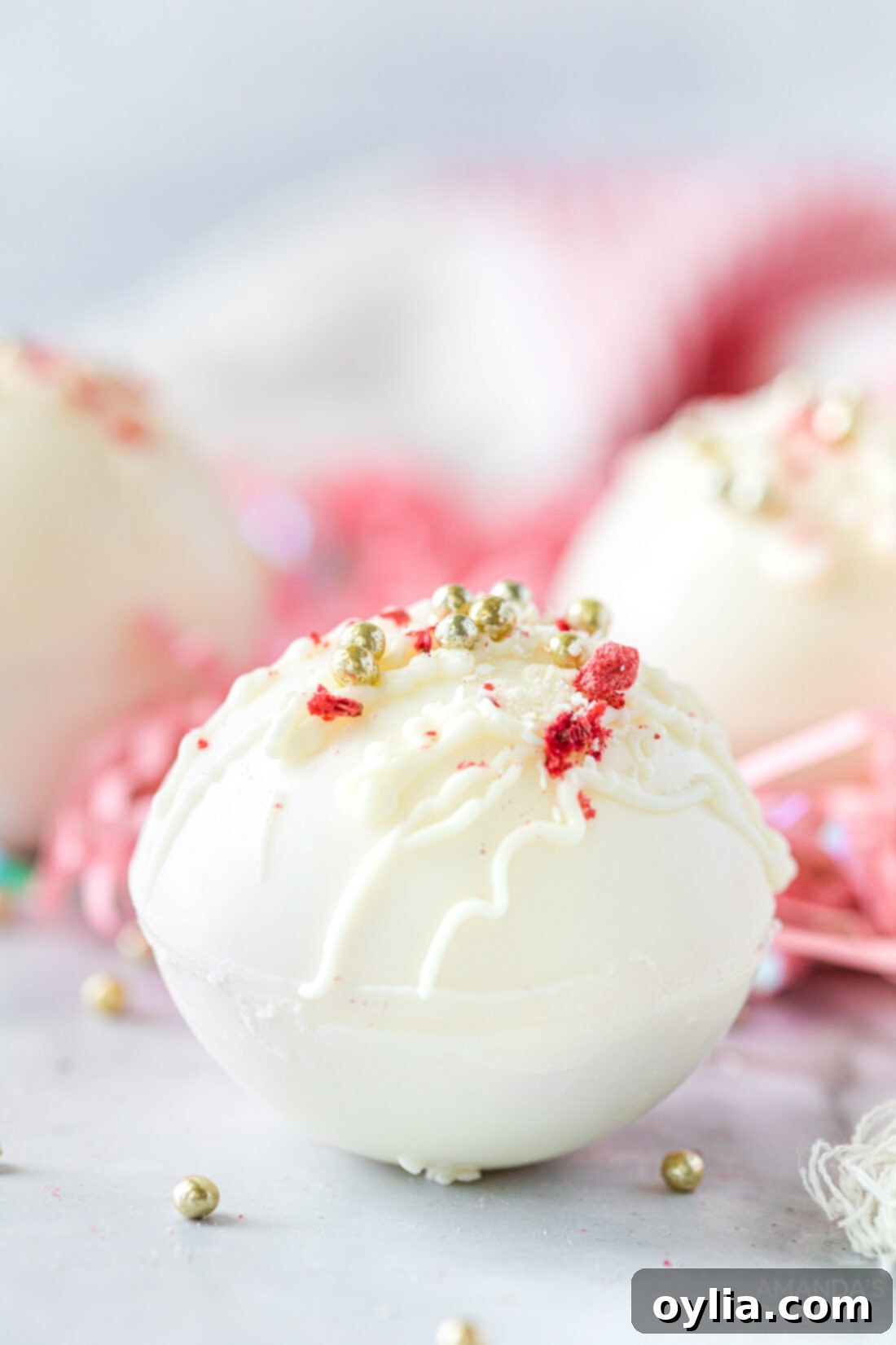 Indulgent Strawberry White Chocolate Hot Cocoa Bombs 16 A display of beautifully decorated white chocolate hot cocoa bombs, adorned with strawberry dust, shaved white chocolate, and sprinkles.