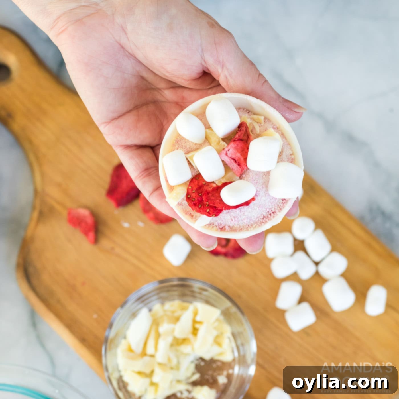 Adding freeze-dried strawberries and mini marshmallows to the filled white chocolate half-sphere.