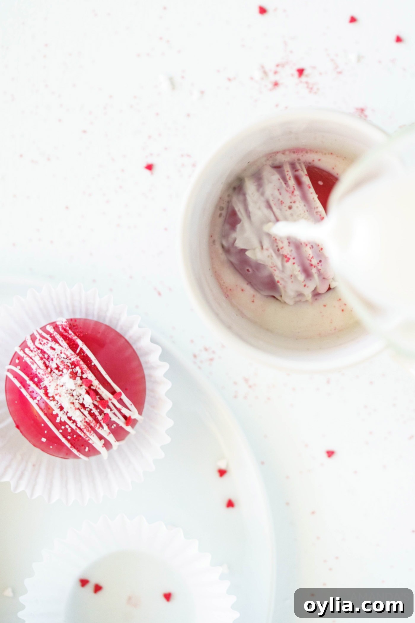 Hot milk is being poured into a mug containing a red velvet hot cocoa bomb, initiating the melting and dissolving process.