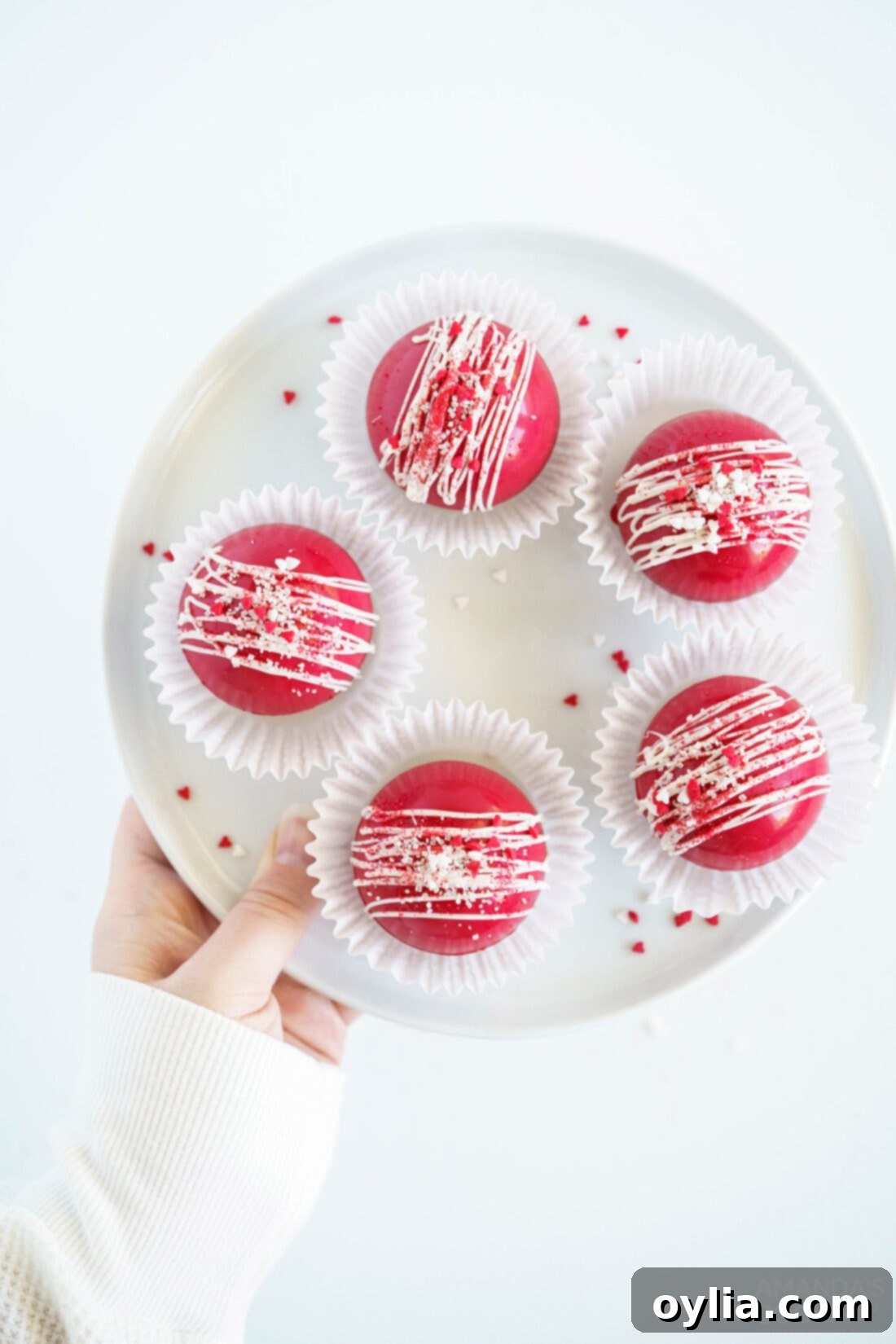 Plate of perfectly formed Red Velvet Hot Cocoa Bombs resting in white paper liners, ready for gifting or serving.