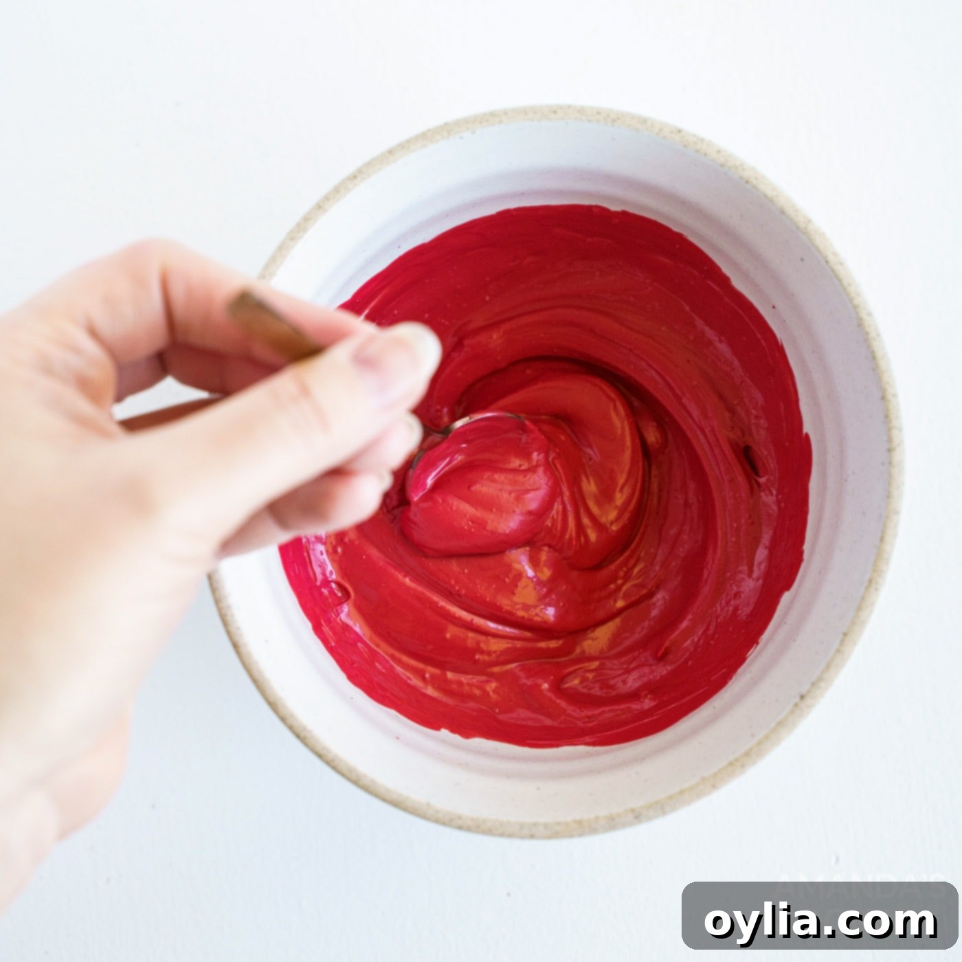 A close-up image of red candy melts being stirred in a bowl over a double boiler until perfectly smooth and melted.