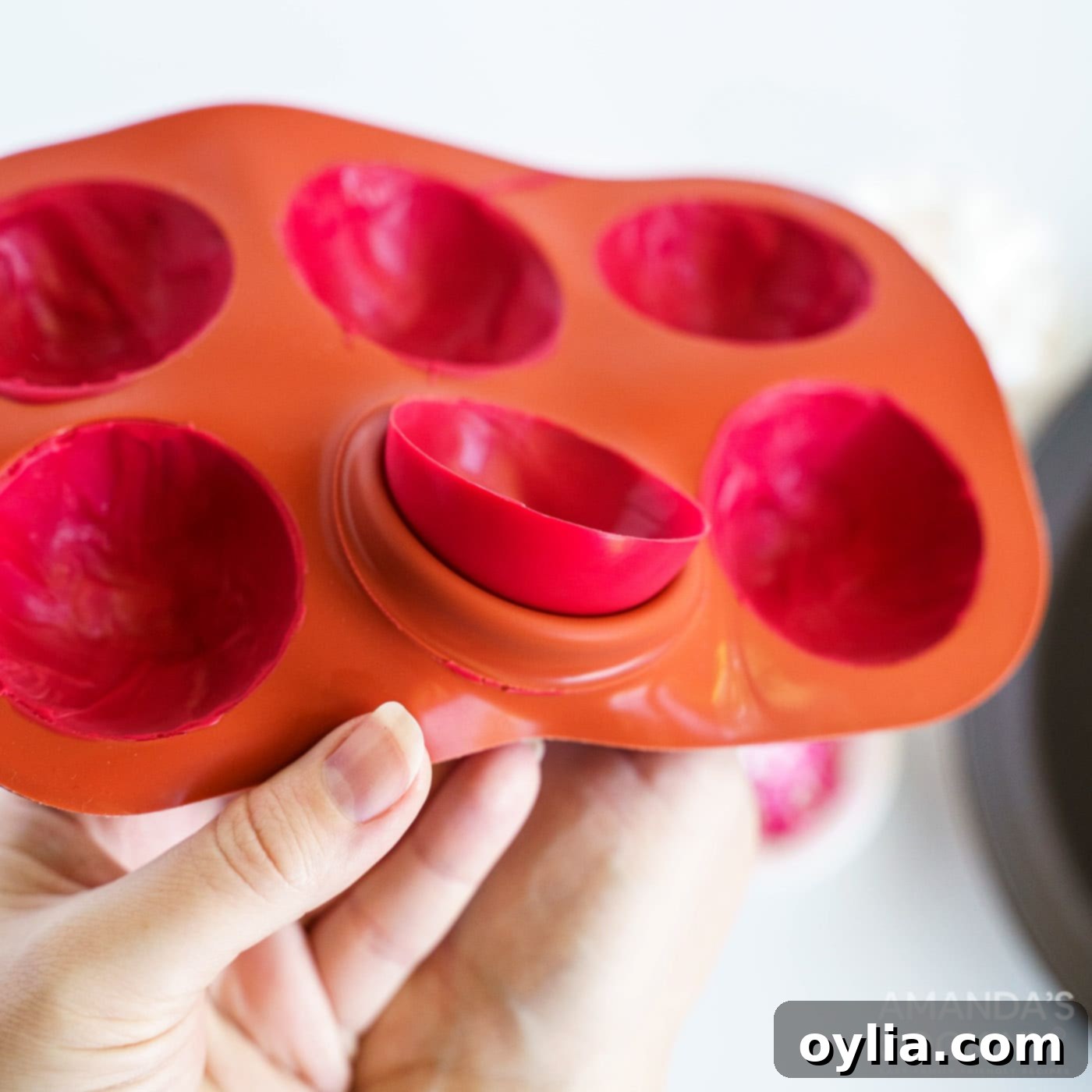 A hand is carefully removing a hardened candy half-sphere from a silicone mold, demonstrating the ease of release.