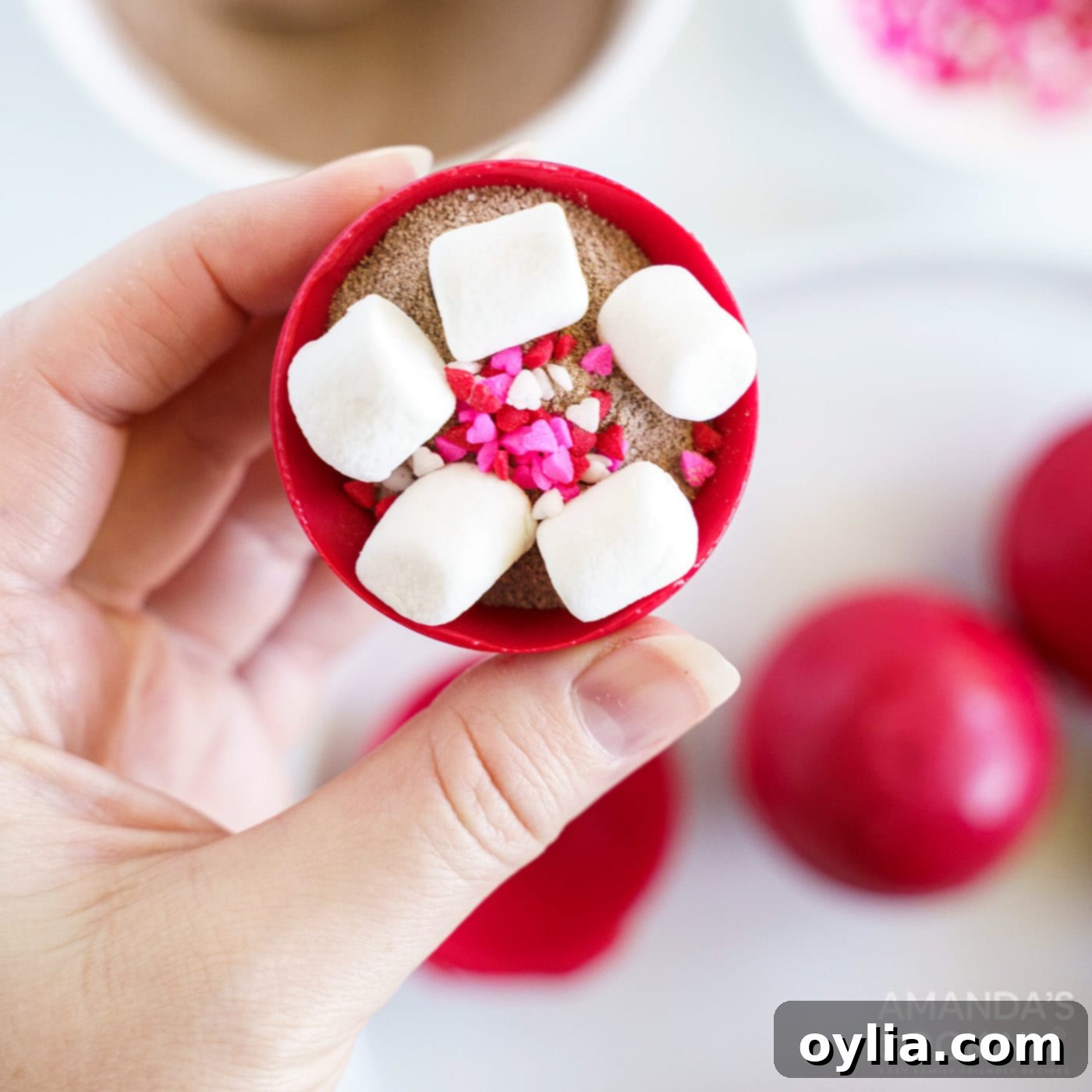 A filled candy half-sphere, revealing hot cocoa mix, mini marshmallows, and heart sprinkles nestled inside, ready to be sealed.
