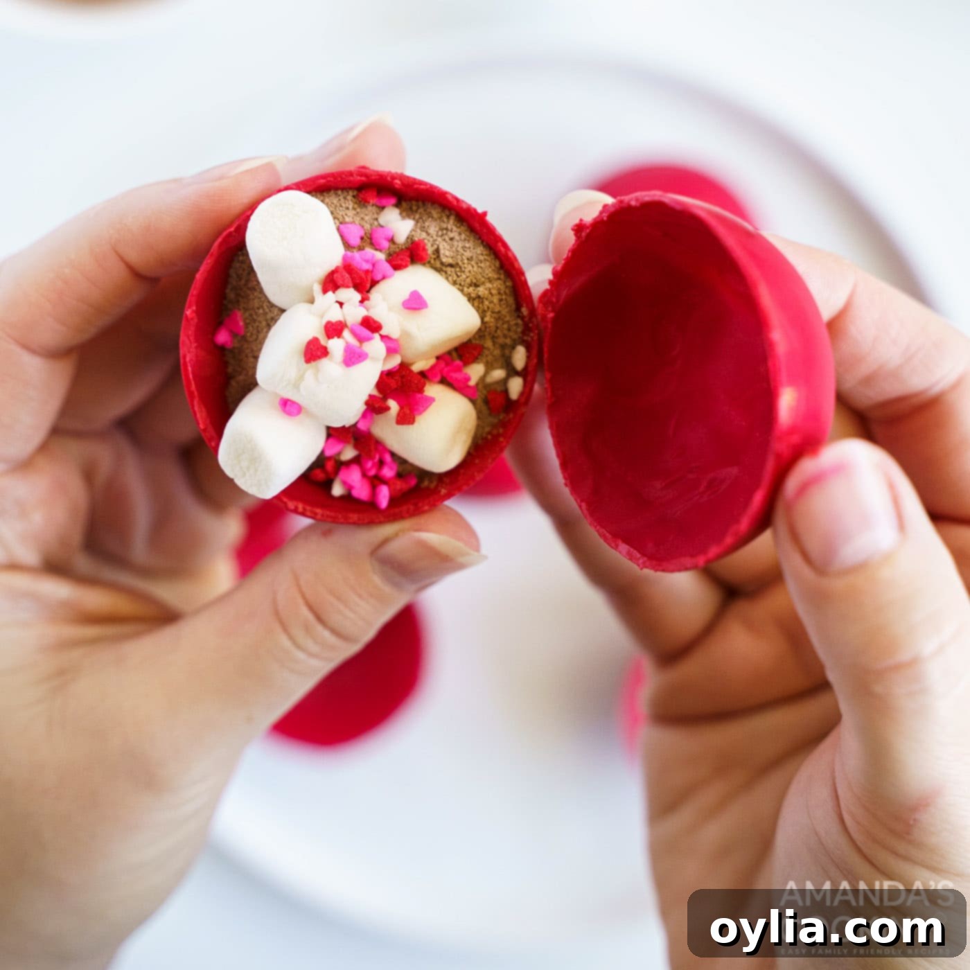Two halves of a hot cocoa bomb are being carefully sealed together, with a finger smoothing the melted candy edges.
