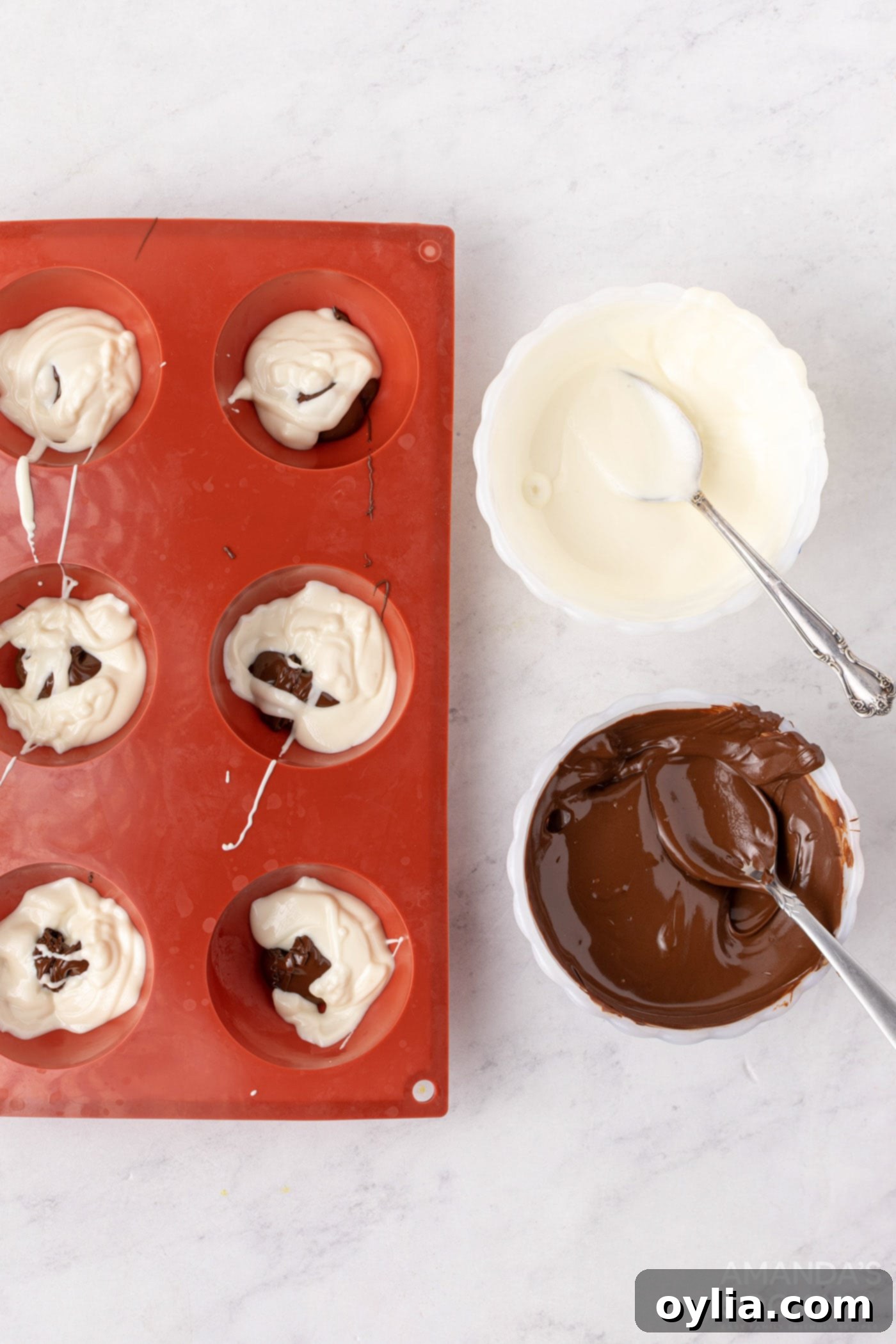 Adding melted semi-sweet and white chocolate to silicone half-sphere molds, creating a marbled pattern as they are swirled.