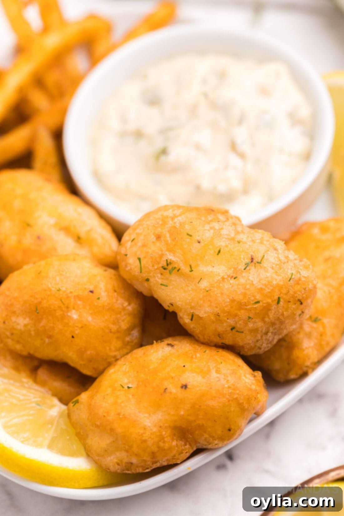 Crispy beer battered fish nuggets served on a plate with homemade tartar sauce and lemon wedges