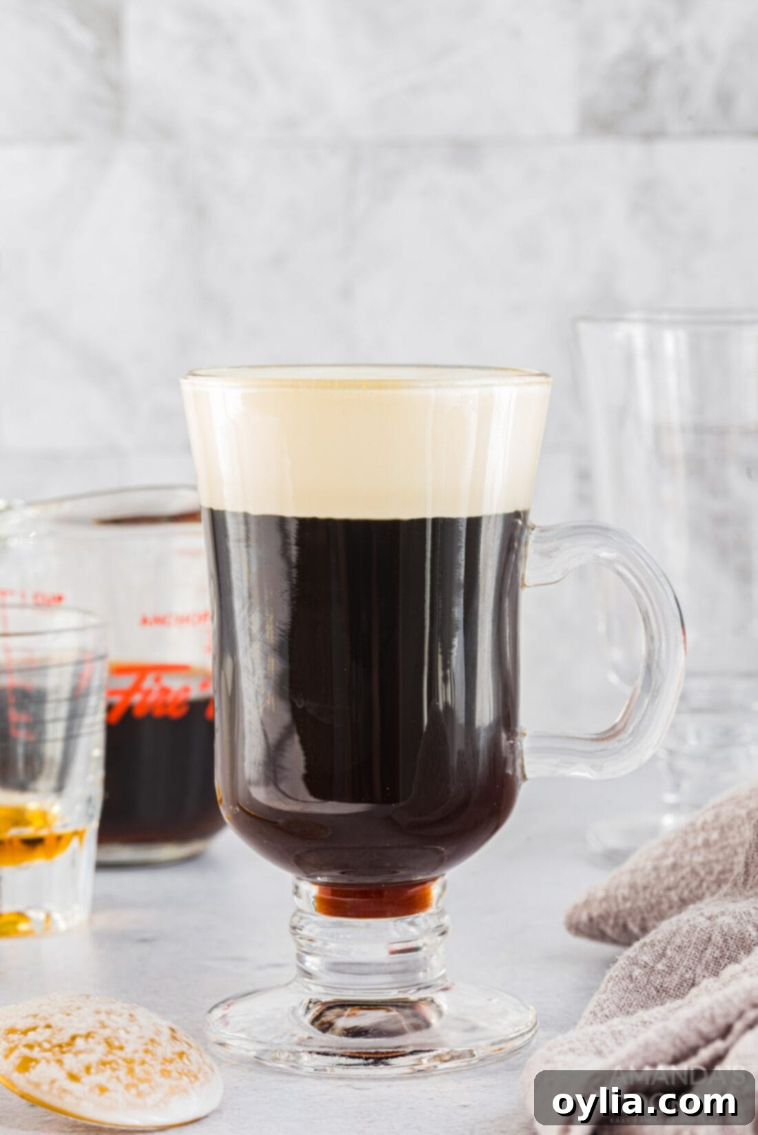 A perfectly prepared glass mug of Irish coffee, showcasing the distinct layers of dark coffee, a hint of amber whiskey, and a fluffy white cream topping.