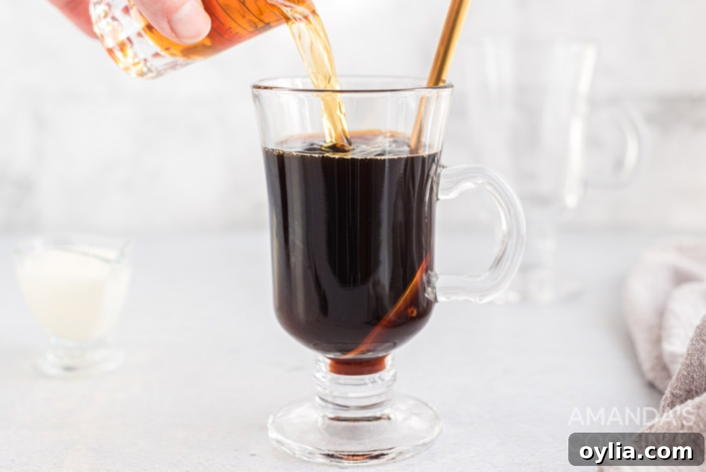 A shot of Irish whiskey being poured into the sweetened coffee in a glass mug.
