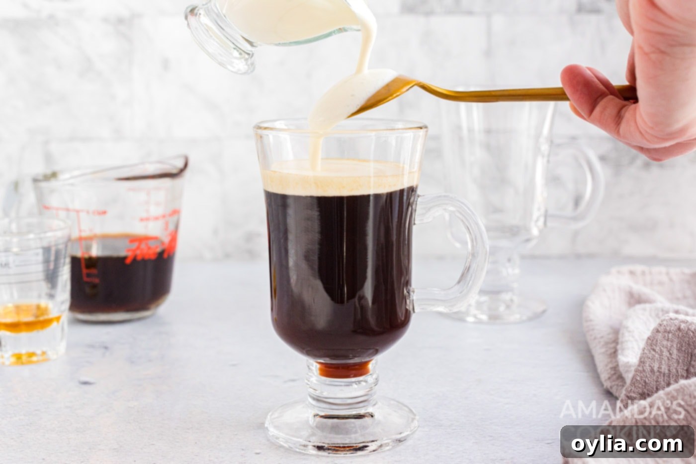 Lightly whipped heavy cream being gently poured over the back of a spoon onto the Irish coffee, ensuring it floats.