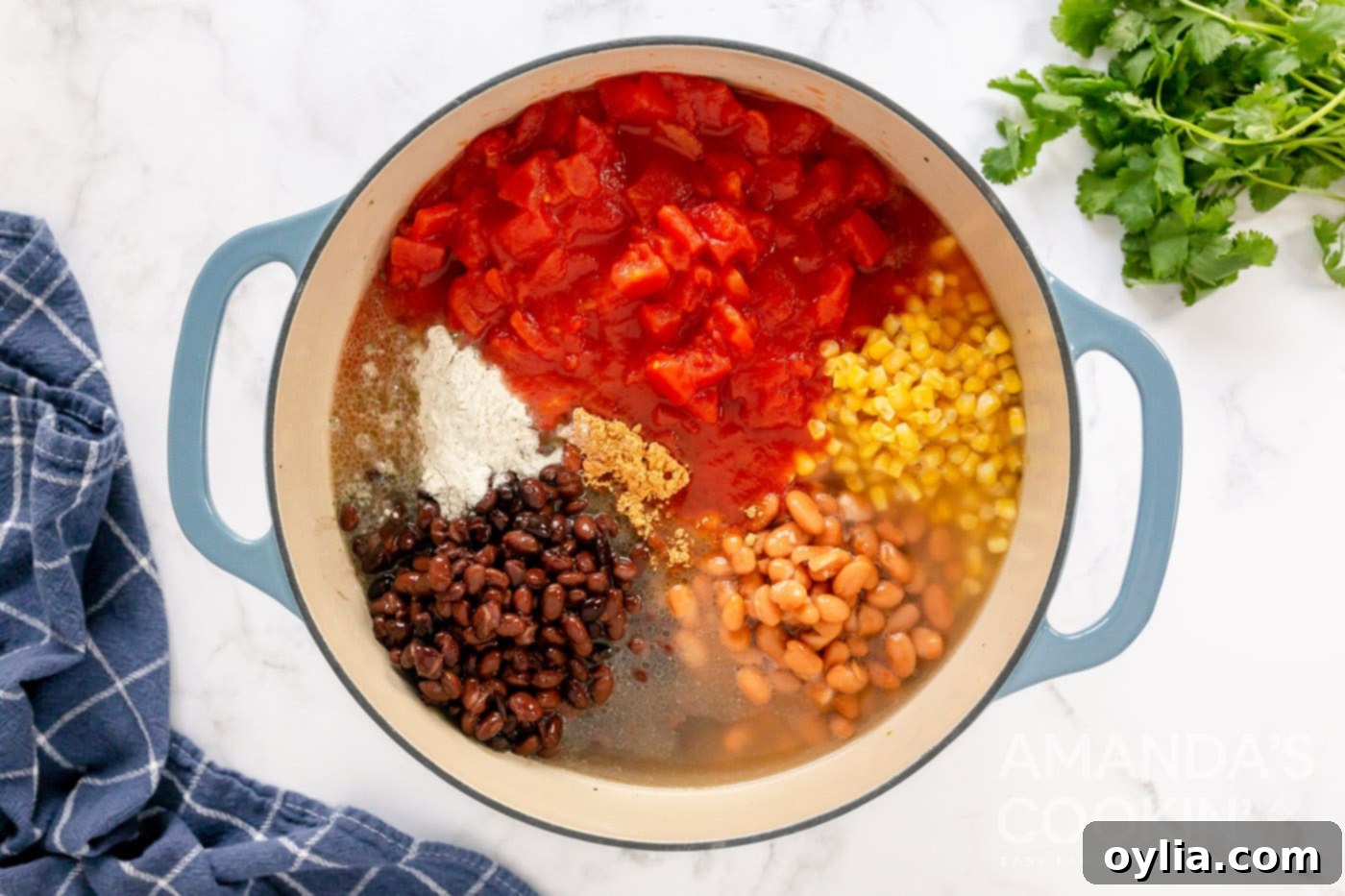 A large pot filled with all the taco soup ingredients including chiles, beans, broth, seasoning, corn, and diced tomatoes, stirred together before simmering.