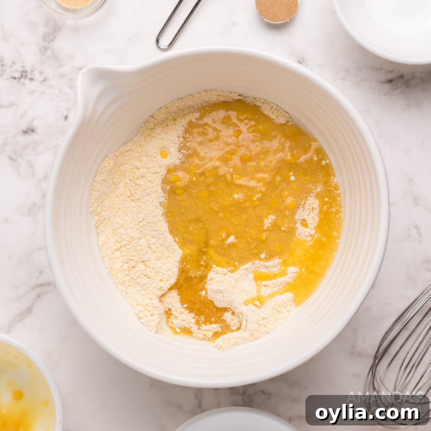 Cream corn and canola oil being added to the cornbread mixture in a bowl.