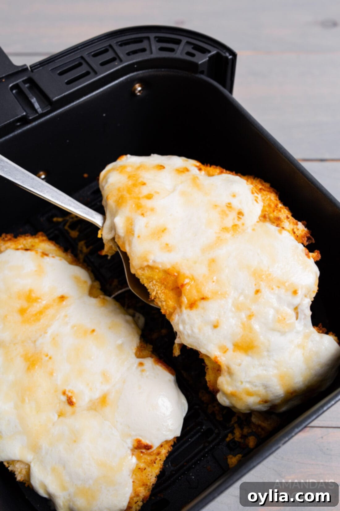 Crispy Air Fryer Chicken Parmesan 3 Removing a perfectly cooked air fryer chicken parmesan cutlet from the air fryer basket with tongs, showing its golden crispness.