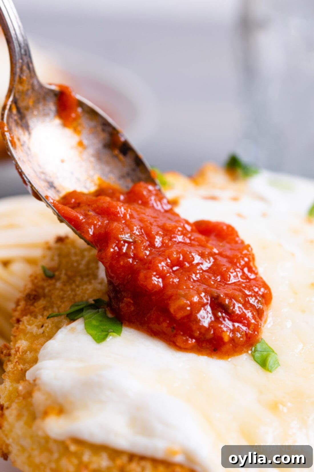 Crispy Air Fryer Chicken Parmesan 4 A hand spooning rich marinara sauce over a crispy air fried chicken cutlet, preparing it for a second bake with cheese.