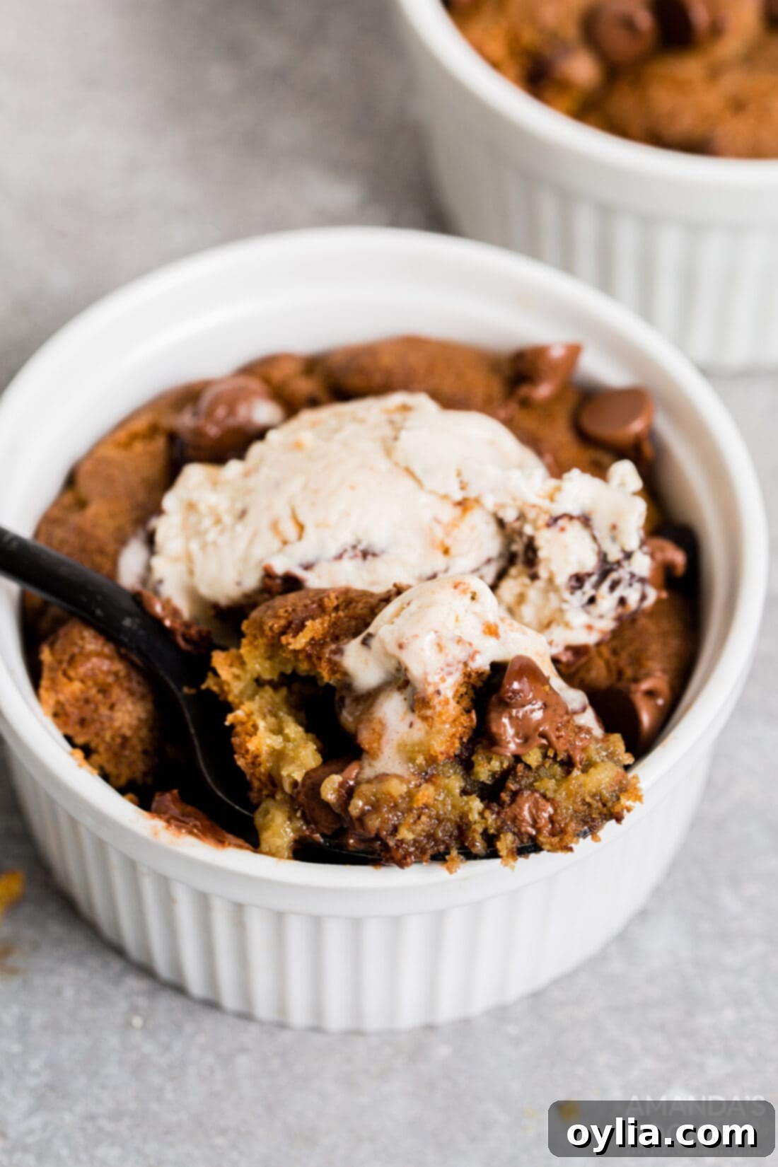 An air fryer chocolate chip cookie served in a ramekin with a scoop of melting vanilla ice cream on top, ready to be enjoyed as a dessert sundae.