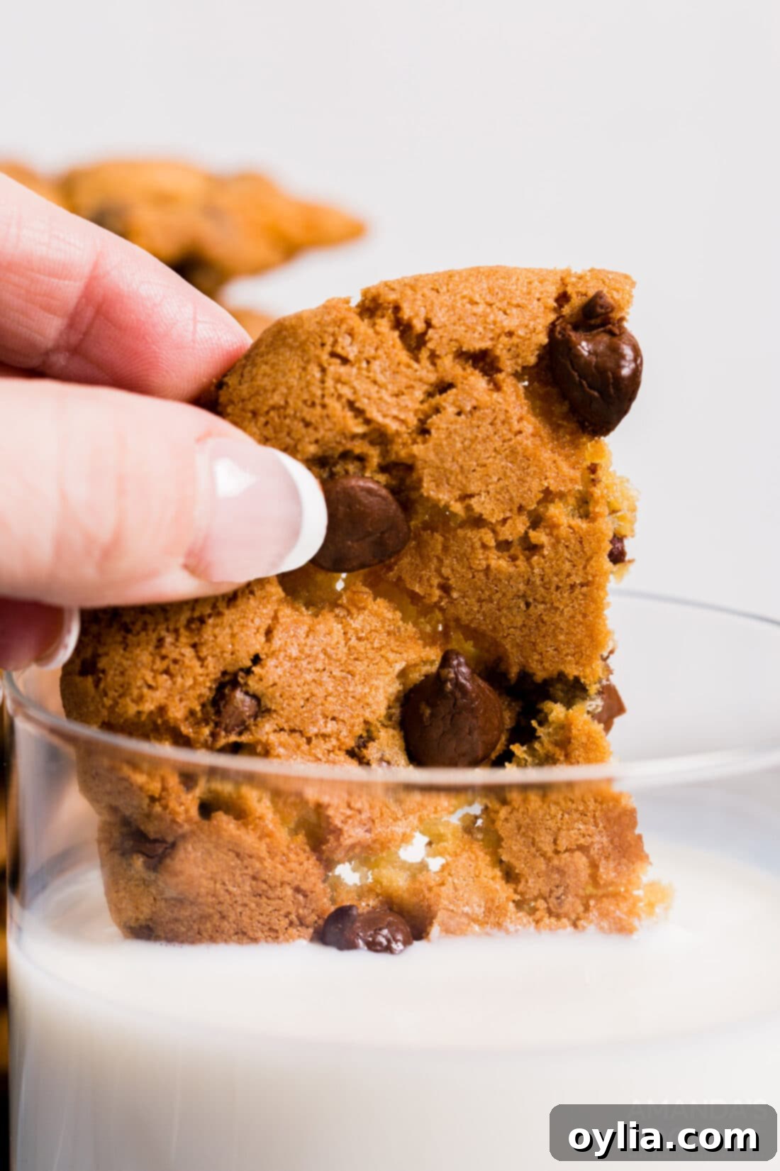 Hand dipping a warm air fryer chocolate chip cookie into a glass of milk, emphasizing its soft, chewy texture.