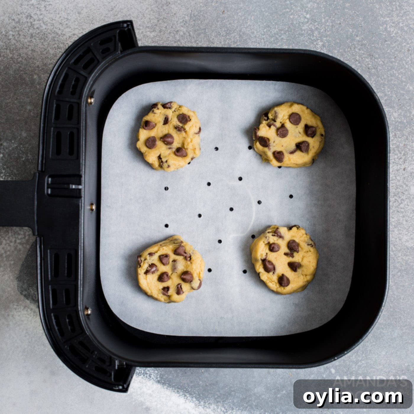 Scooped chocolate chip cookie dough balls placed on parchment paper in an air fryer basket.