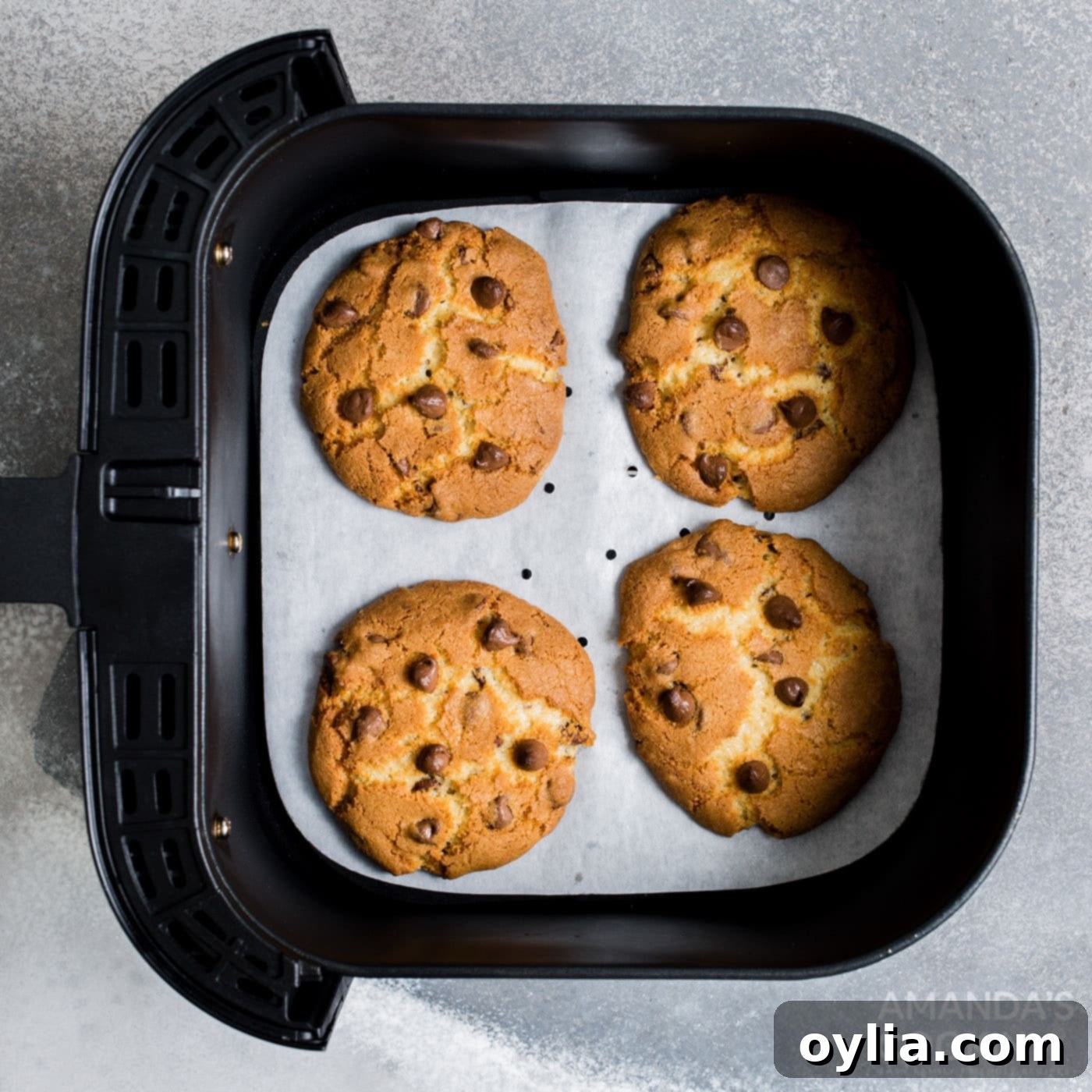 Warm chocolate chip cookies cooling in the air fryer basket after baking.