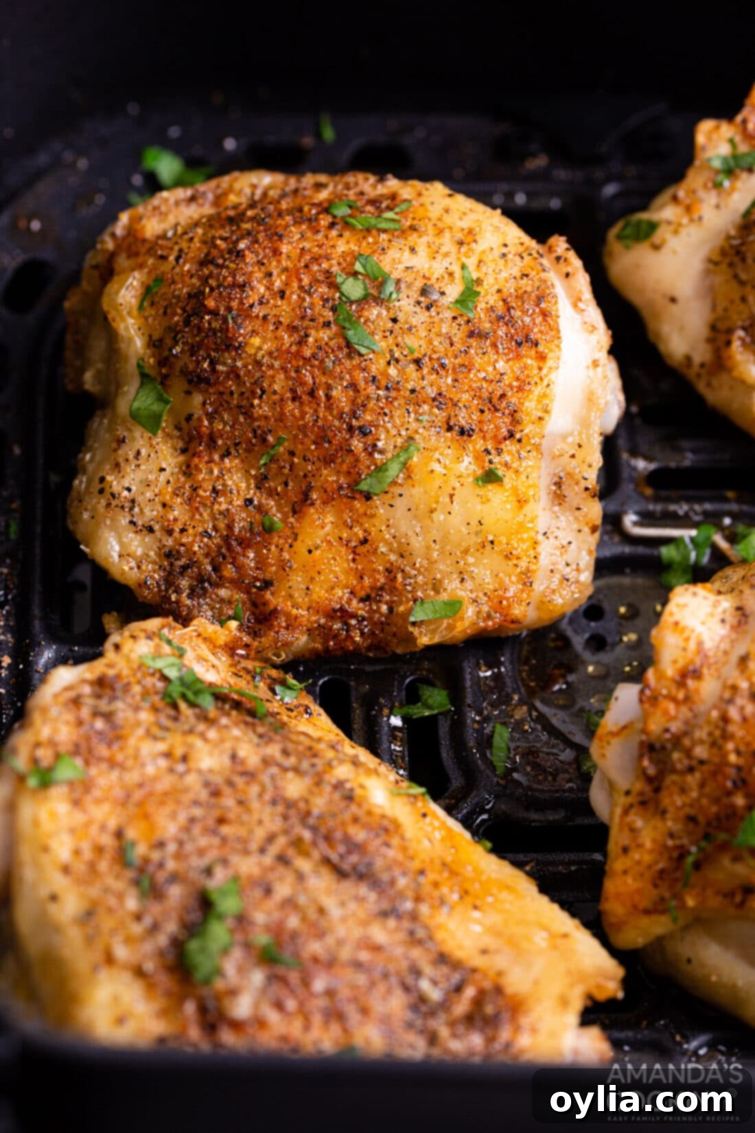 Crispy Air Fryer Chicken Thighs 2 cooked chicken thighs in an air fryer basket, golden brown and crispy