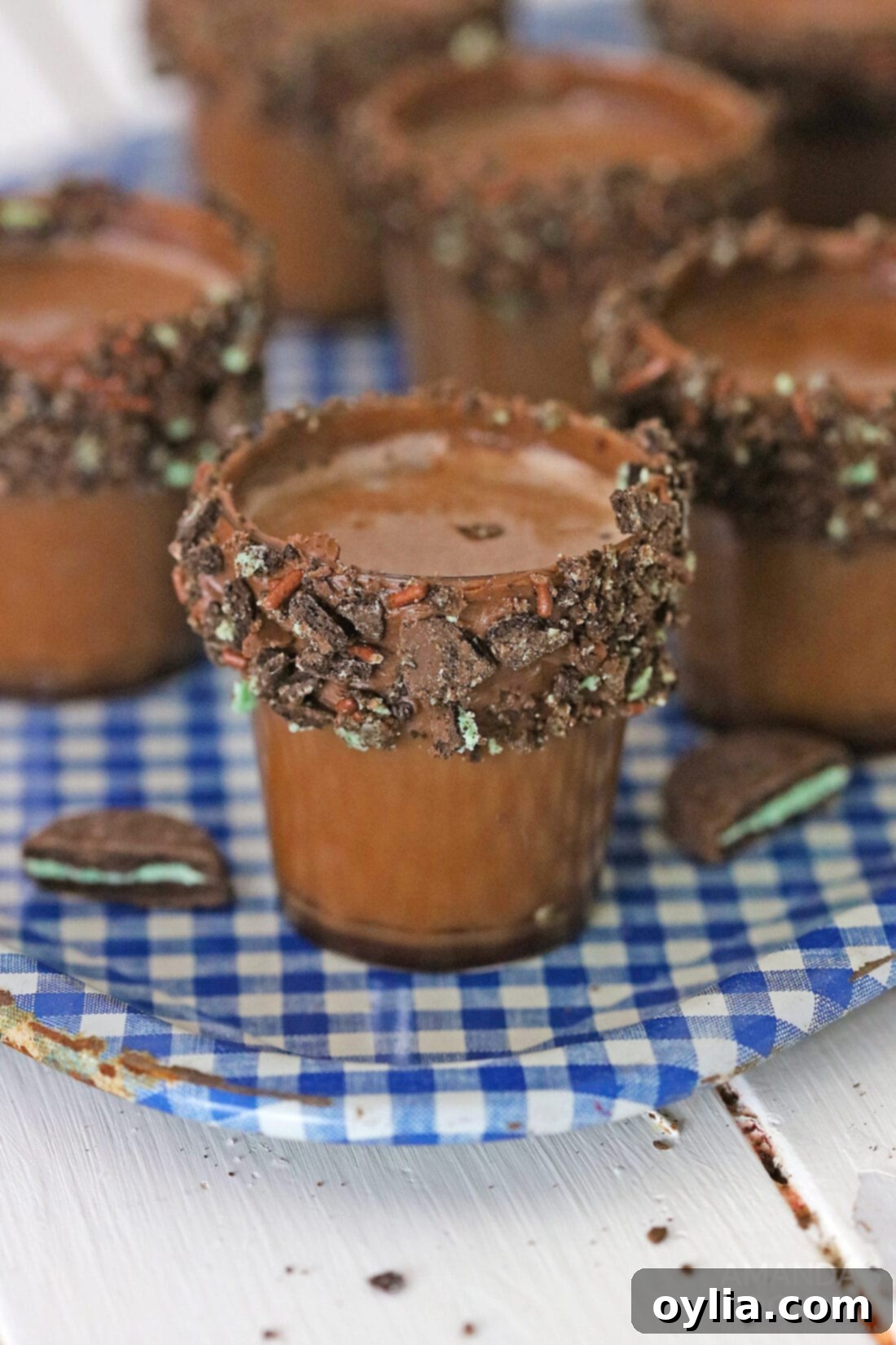 Shot glasses filled with chocolate mint cocktail, garnished with crushed Oreo Thin Mint cookies, arranged on a blue tray.