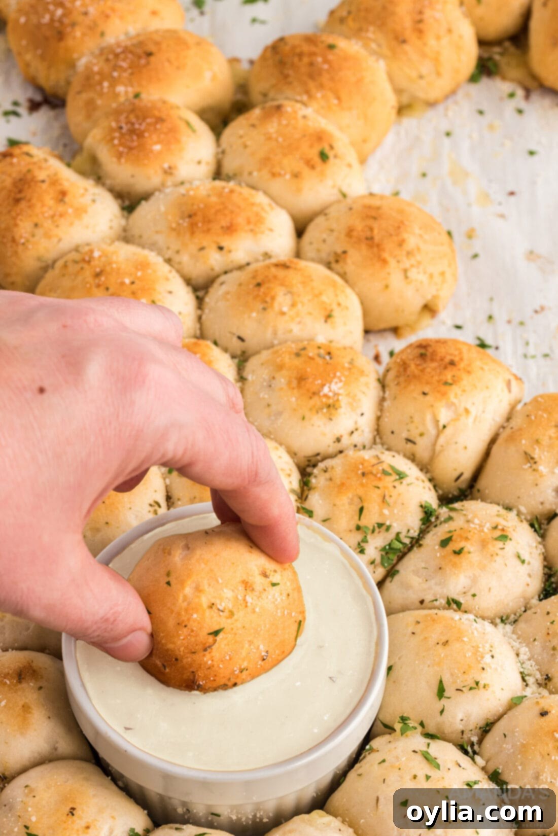 A hand dipping a cheese-filled bread ball from the Easter bunny pull apart bread into ranch dressing.
