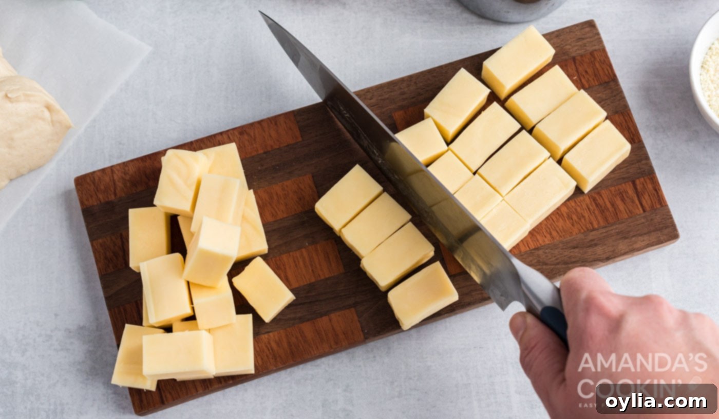 A hand cutting a block of mozzarella cheese into small cubes for filling the biscuits.