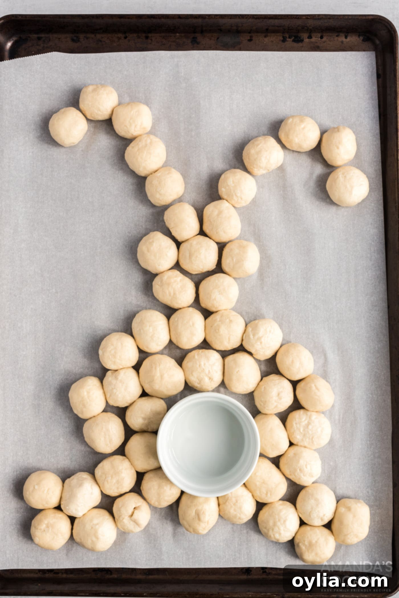 Biscuit balls arranged on a parchment-lined baking sheet in the shape of a bunny rabbit with a ramekin for the tail.