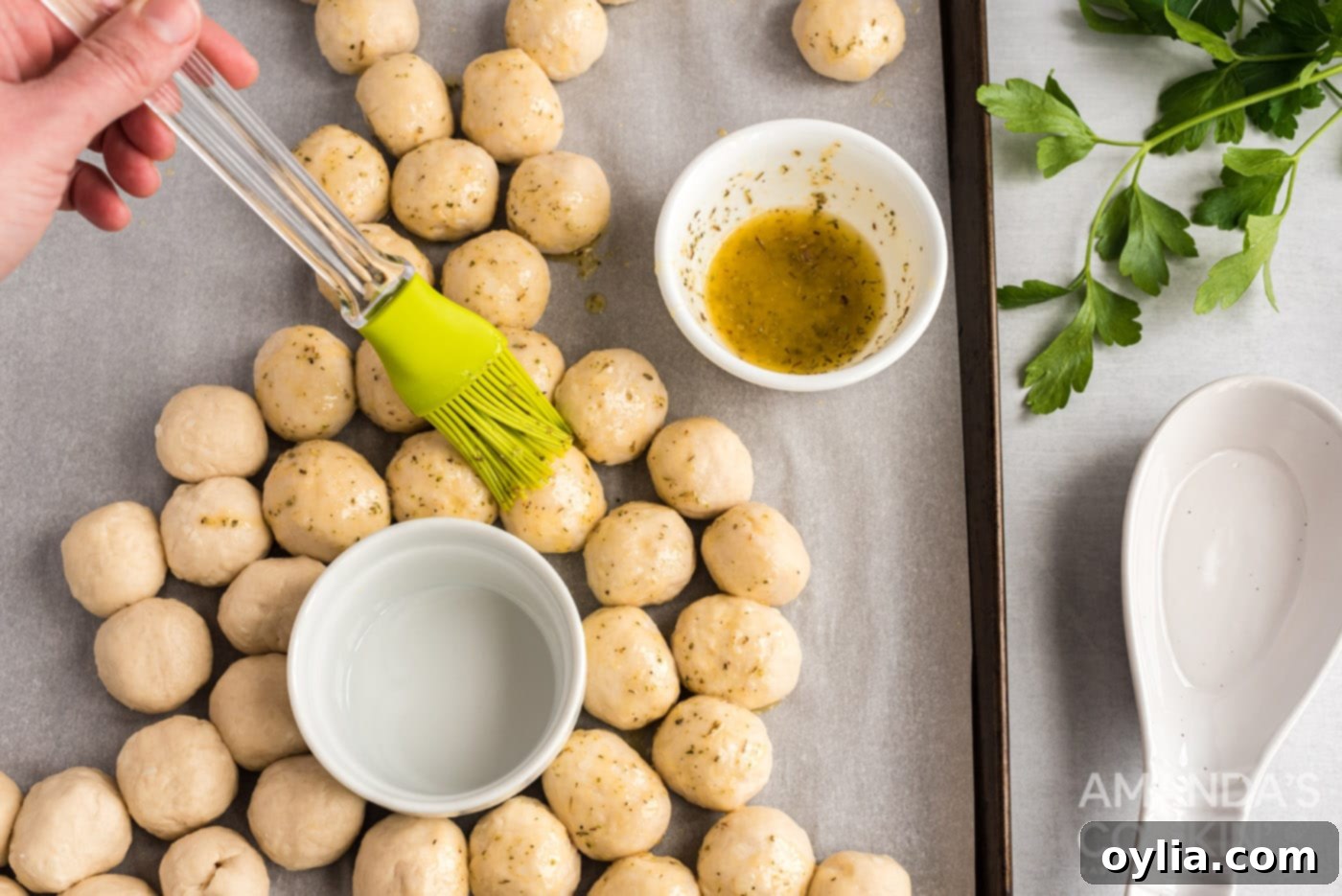 A pastry brush applying melted butter with herbs over the unbaked biscuit balls arranged as a bunny.