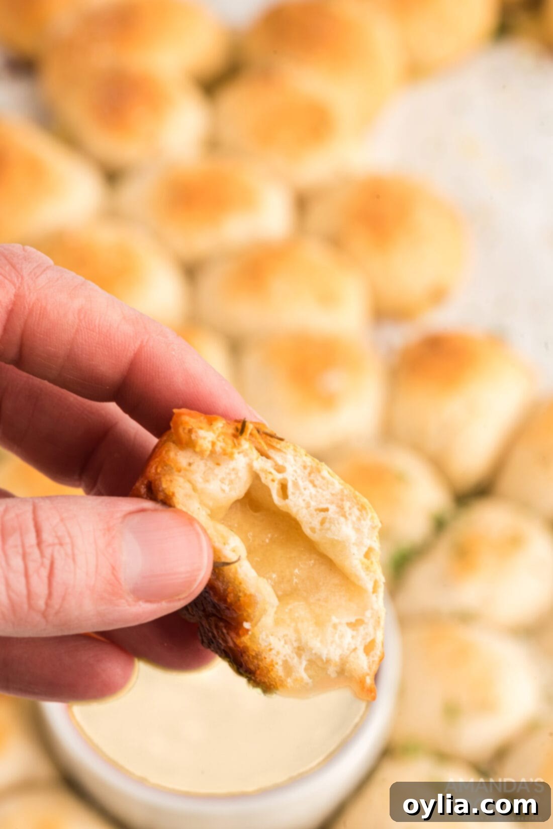 A close-up of a hand pulling a cheesy biscuit ball from the Easter bunny pull apart bread, showing melted cheese.