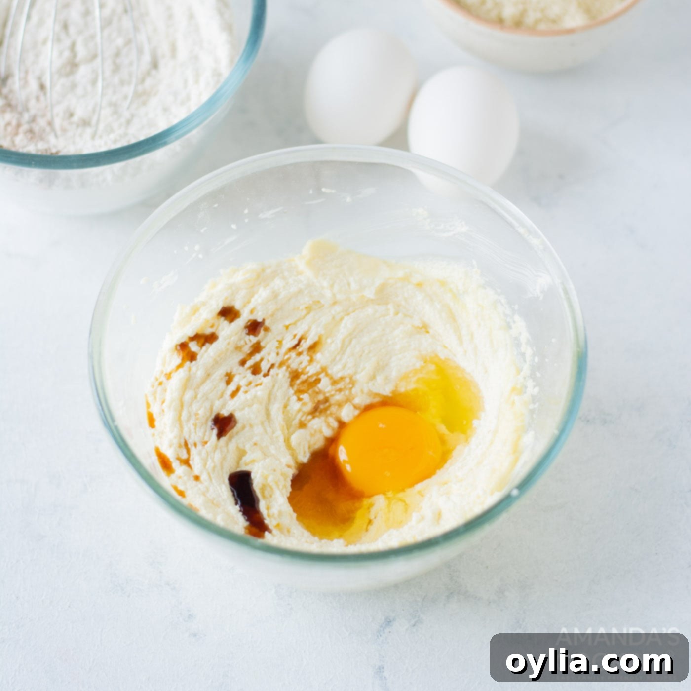 A cracked egg and a splash of vanilla extract being added to the creamy butter and sugar mixture in a bowl, before blending.