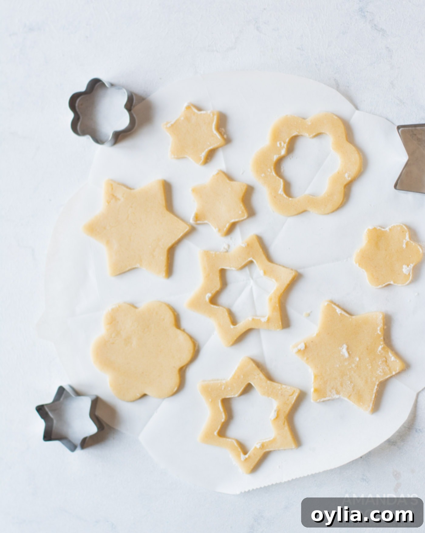 Cookie dough rolled out on a floured surface, with various shapes perfectly cut out using cookie cutters, including those with small centers removed for the top cookie layer.