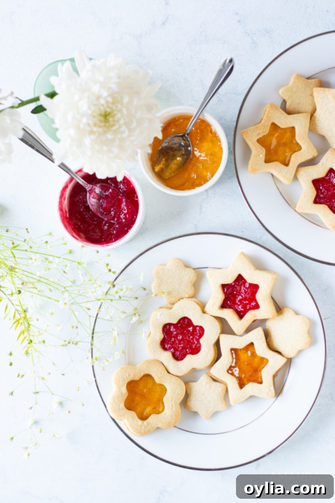 Festive Linzer Sandwich Cookies 10 A close-up view of three beautifully presented Linzer cookies on a white plate, showcasing their rich jam filling, intricate cut-out tops, and delicate powdered sugar dusting.