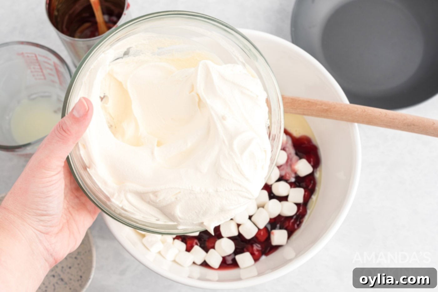 Adding Cool Whip to a mixing bowl with other cherry fluff ingredients.
