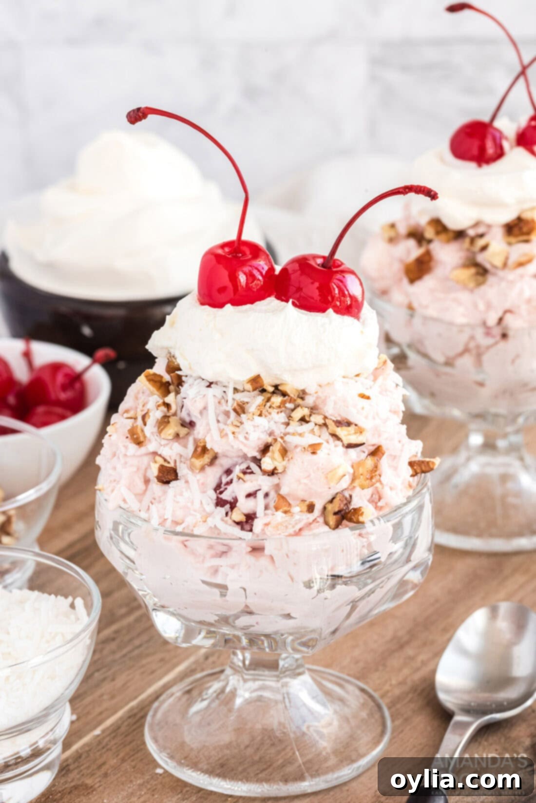 Close-up of a serving of cherry fluff dessert, garnished with chopped nuts, whipped cream, and a maraschino cherry.