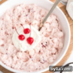 Close up photo of a bowl of Cherry Fluff topped with cool whip and maraschino cherries