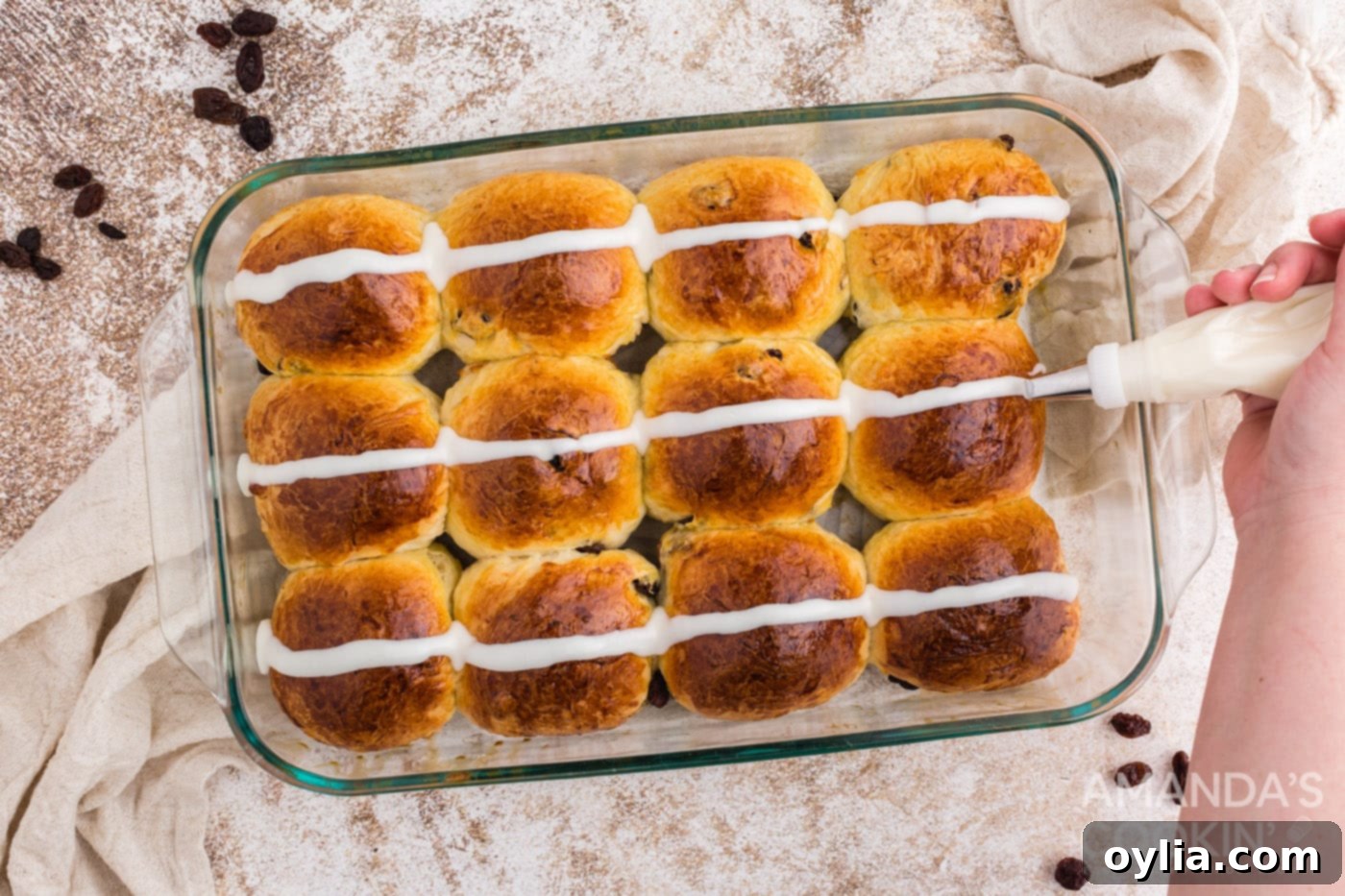 Applying icing strips to warm buns in a pan to create the signature cross