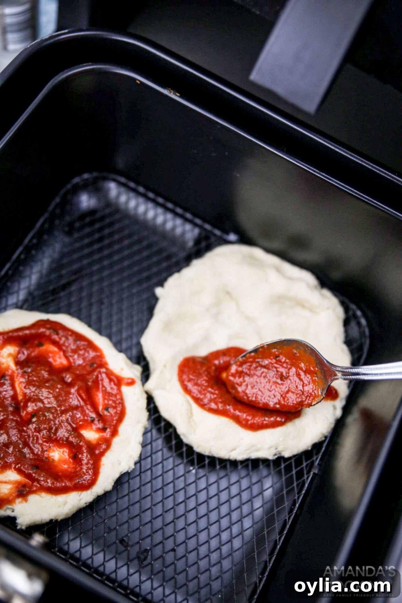 spreading pizza sauce onto the raw pizza crust in the air fryer
