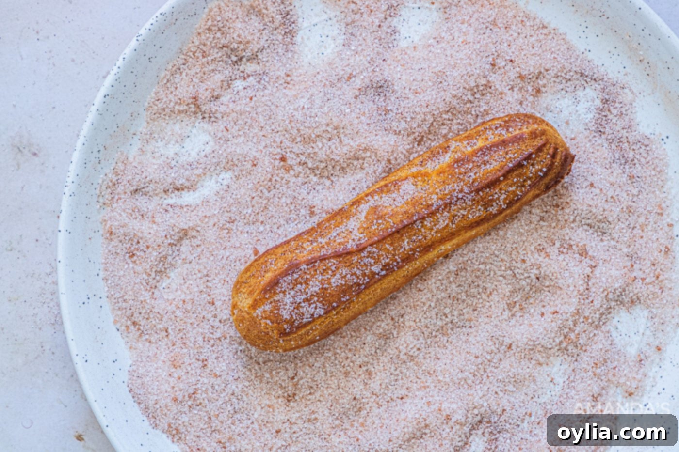 A freshly air-fried churro being tossed in a bowl of cinnamon sugar mixture for coating.