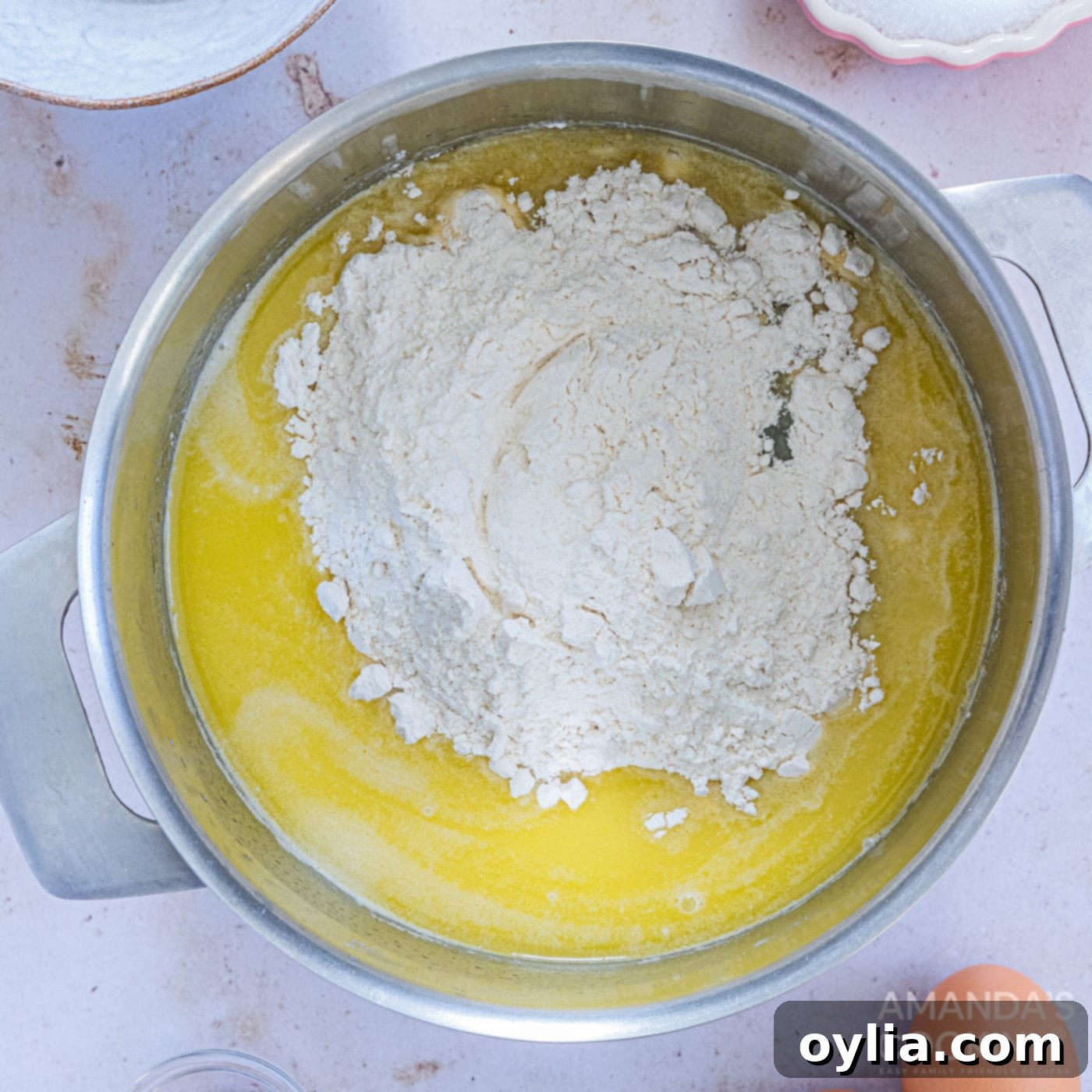 Adding flour to the hot water, butter, sugar, and salt mixture in a saucepan to create the churro dough base.